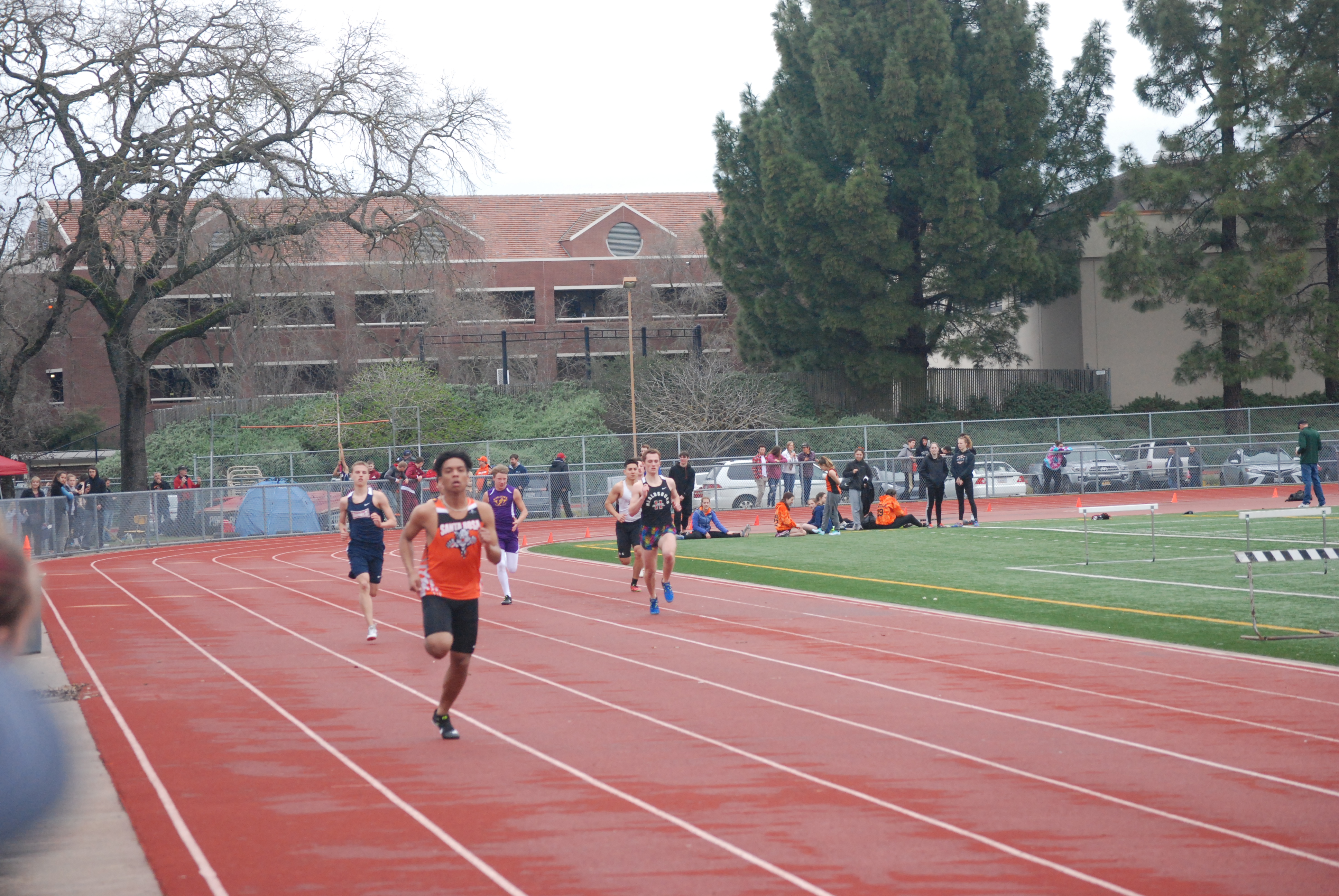 Athlete prepares for pole vault on a track with others watching.