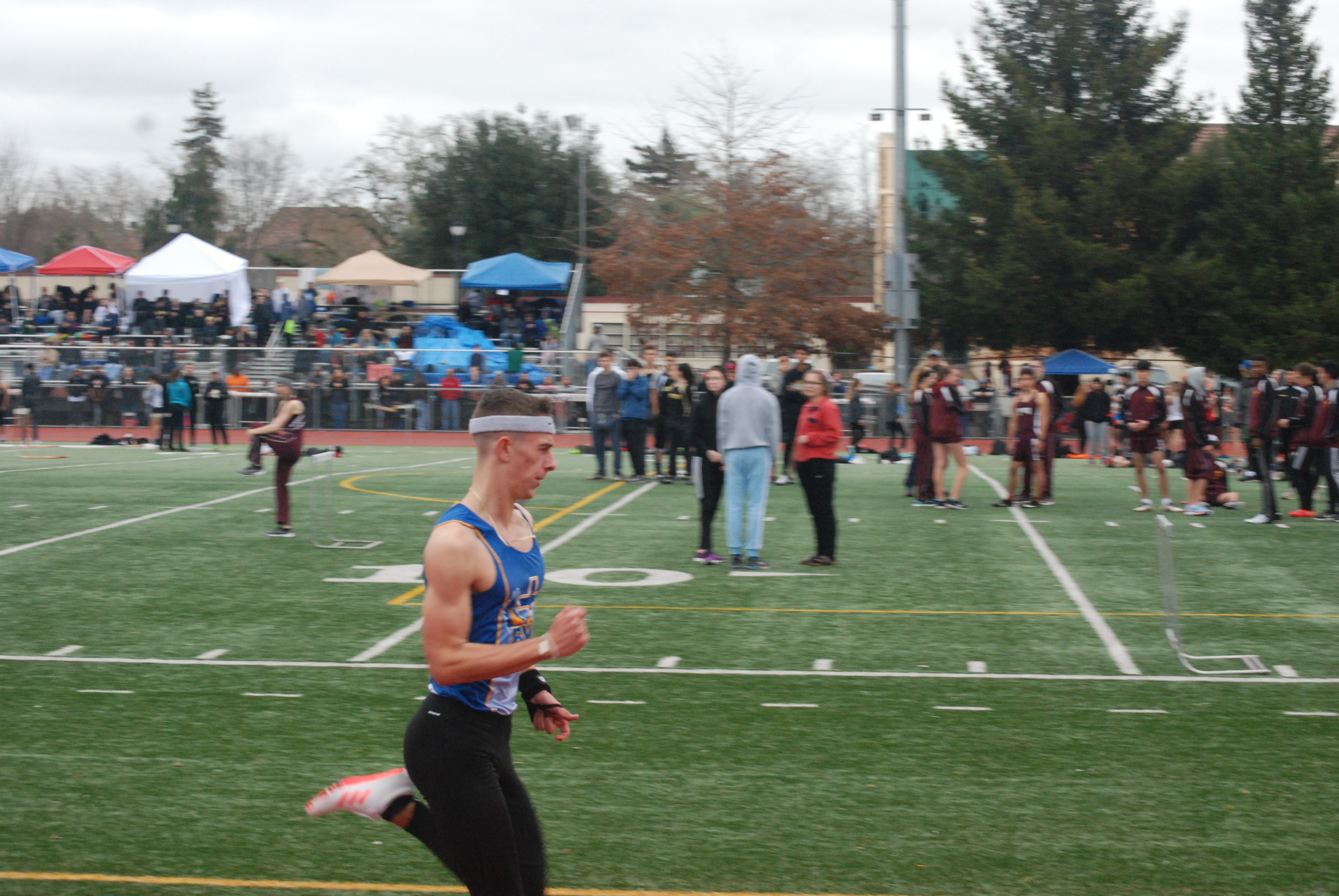 Athlete prepares for pole vault on a track with others watching.