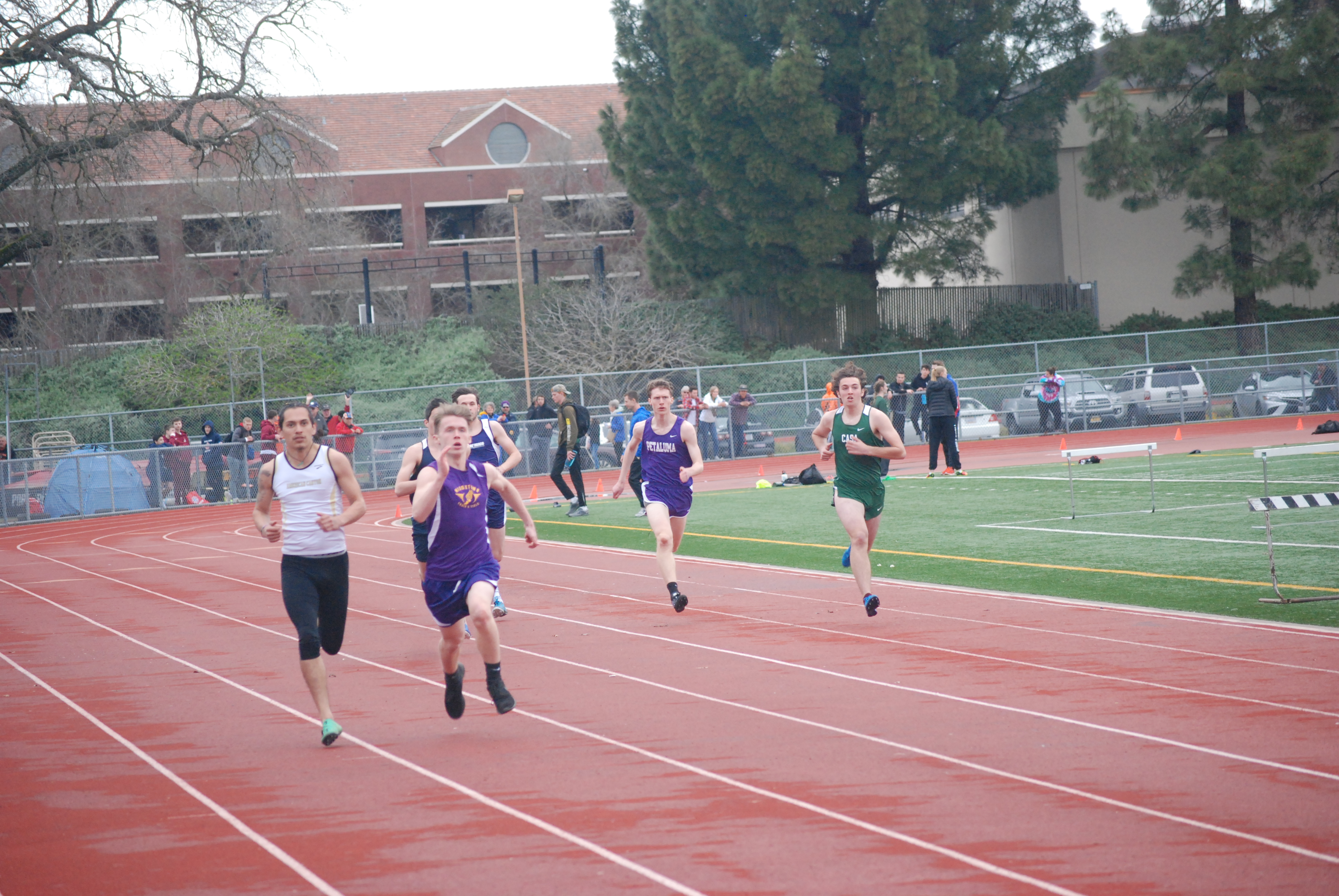 Athlete prepares for pole vault on a track with others watching.