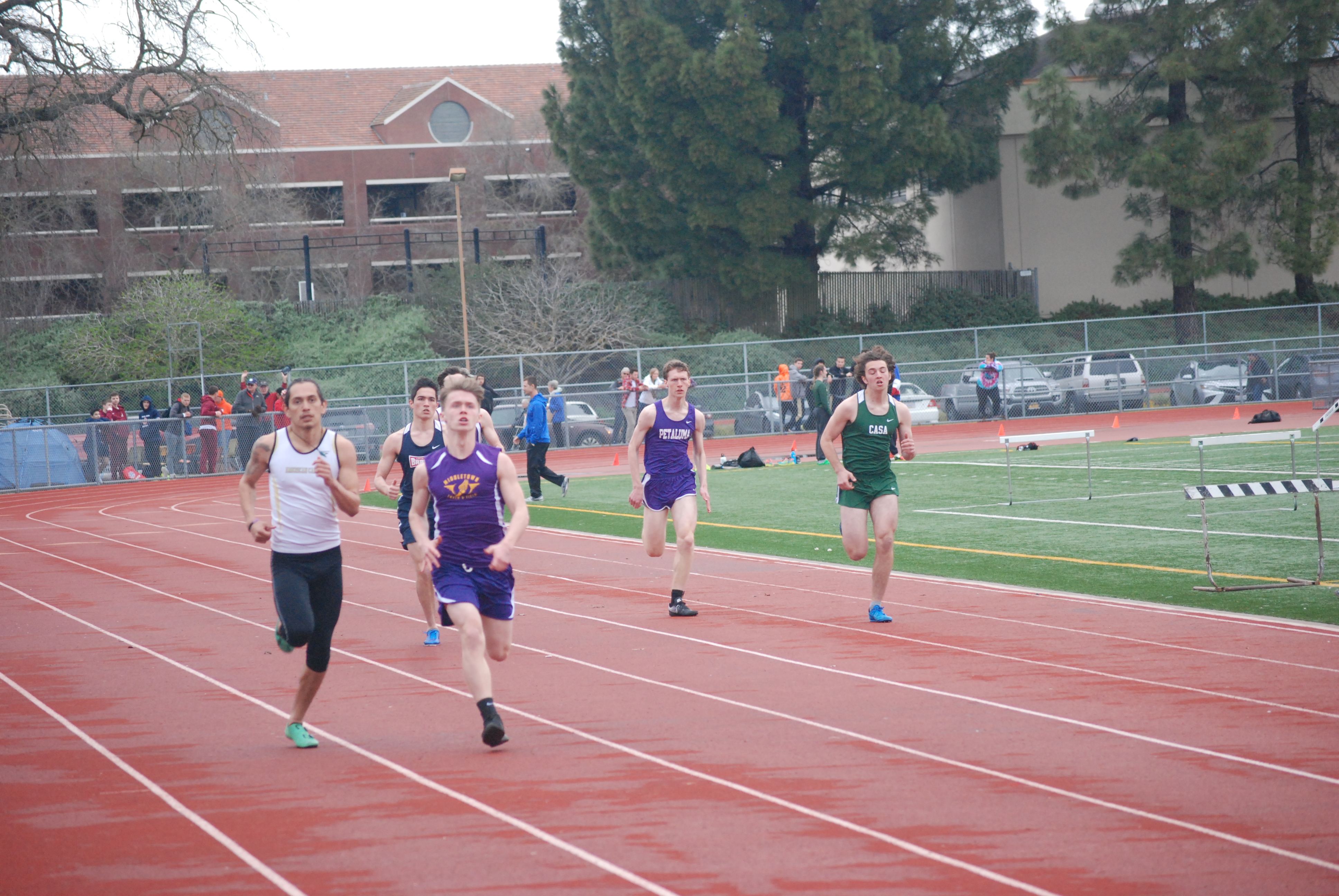 Athlete prepares for pole vault on a track with others watching.