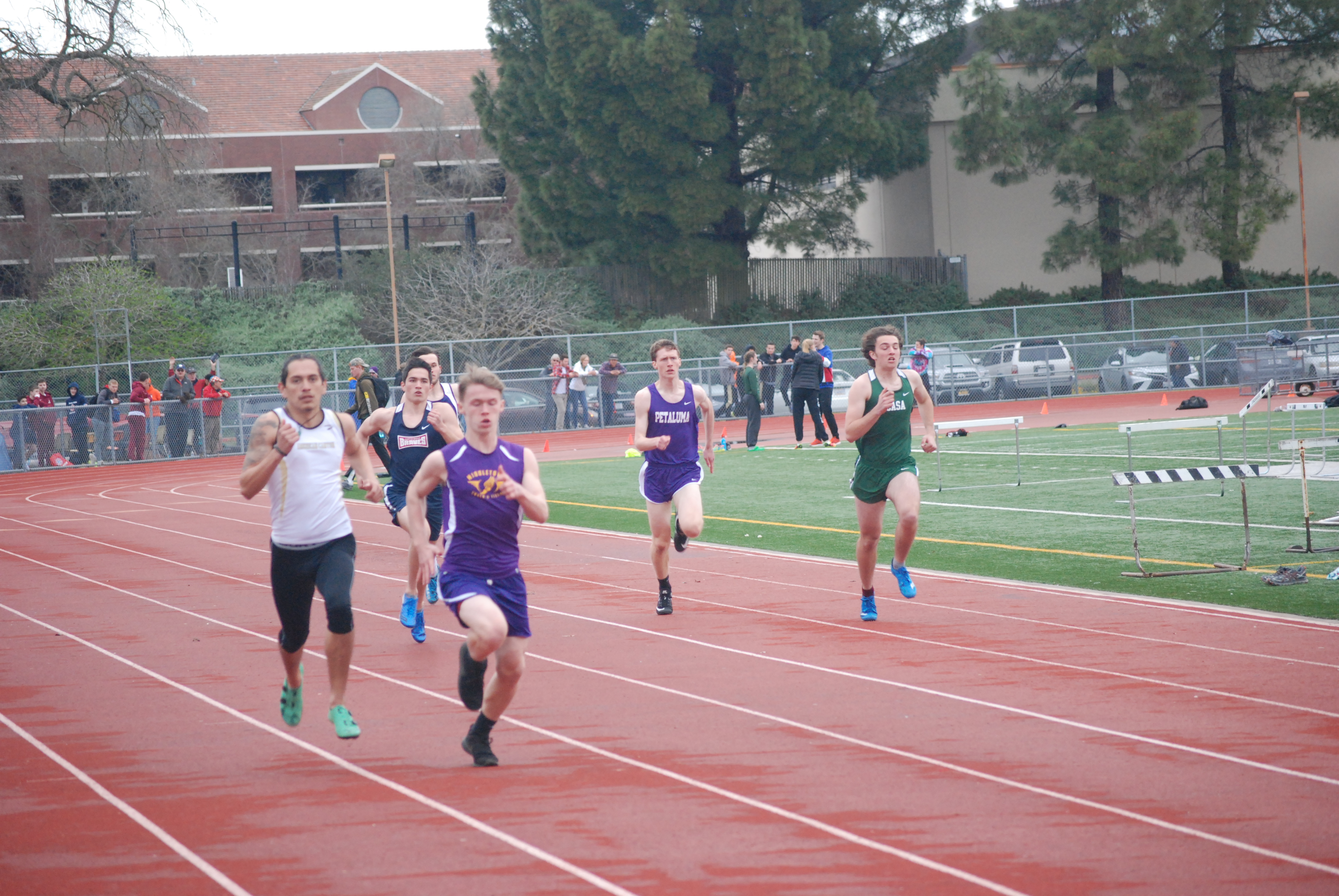 Athlete prepares for pole vault on a track with others watching.