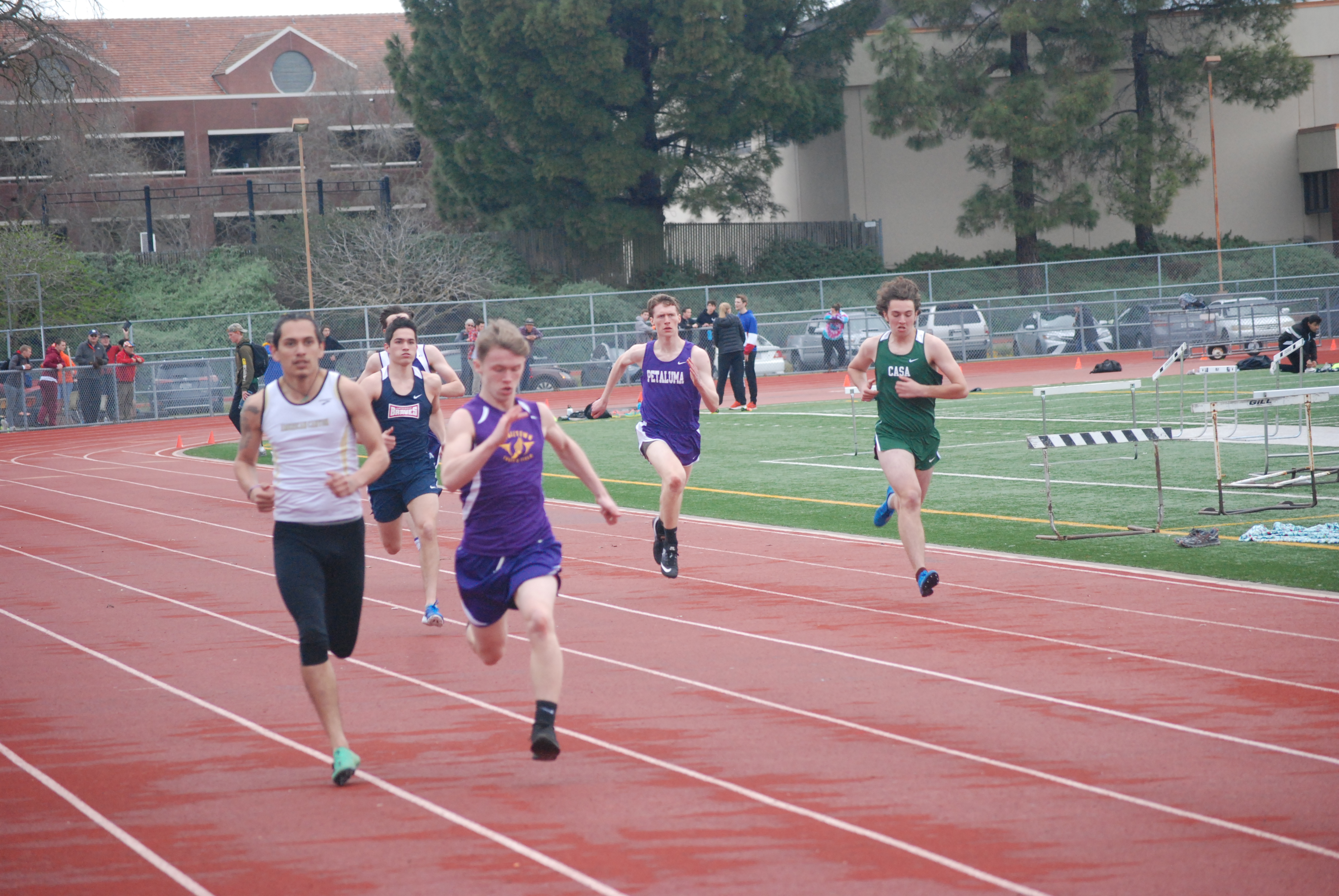 Athlete prepares for pole vault on a track with others watching.