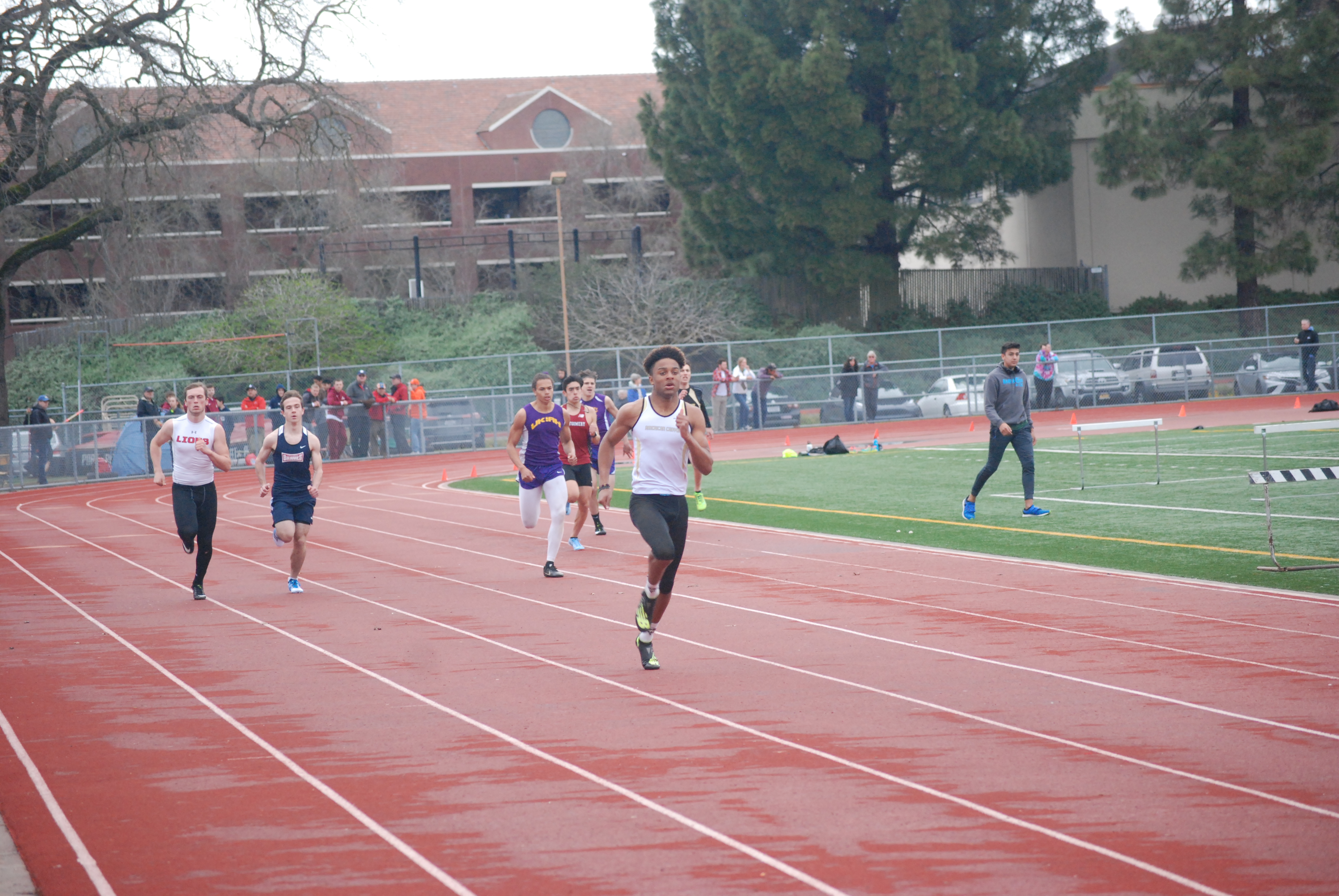 Athlete prepares for pole vault on a track with others watching.