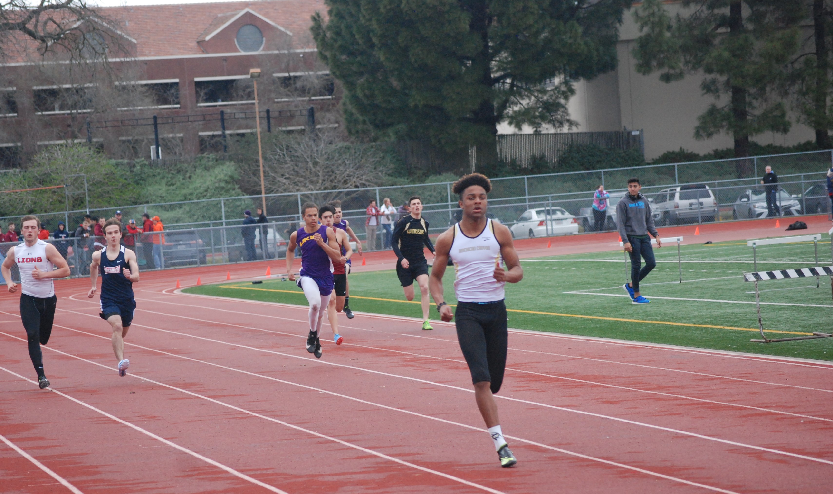 Athlete prepares for pole vault on a track with others watching.