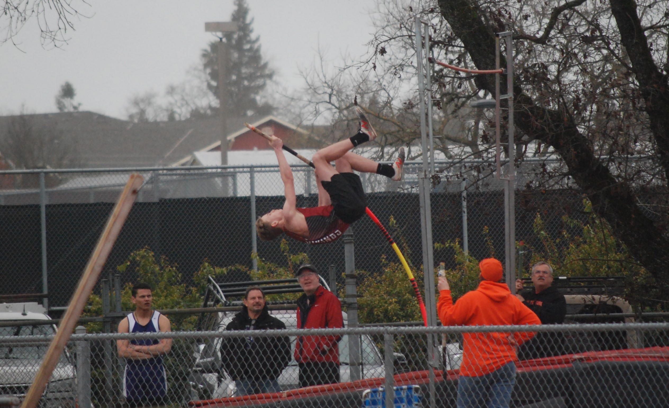 Athlete prepares for pole vault on a track with others watching.