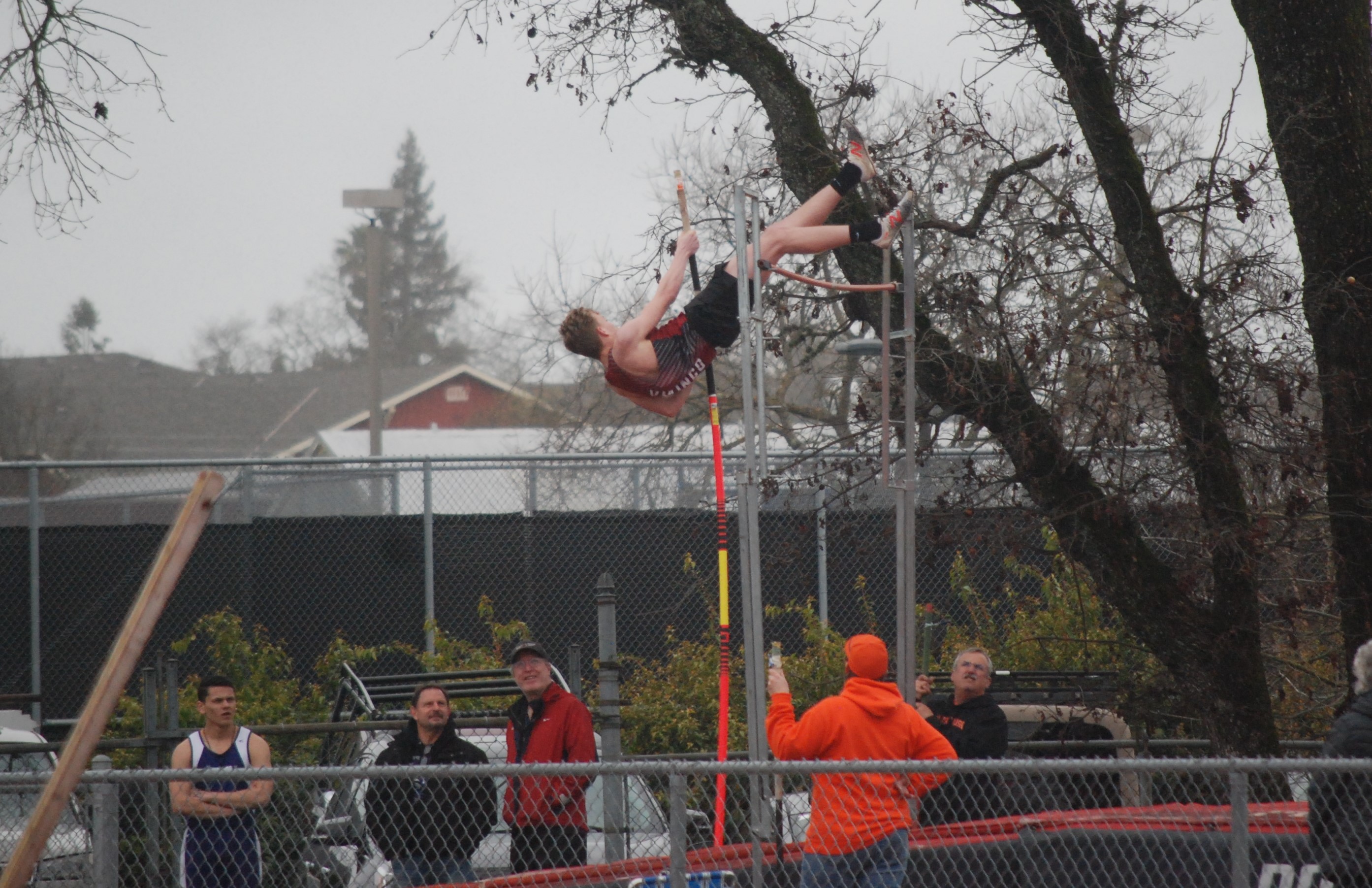 Athlete prepares for pole vault on a track with others watching.