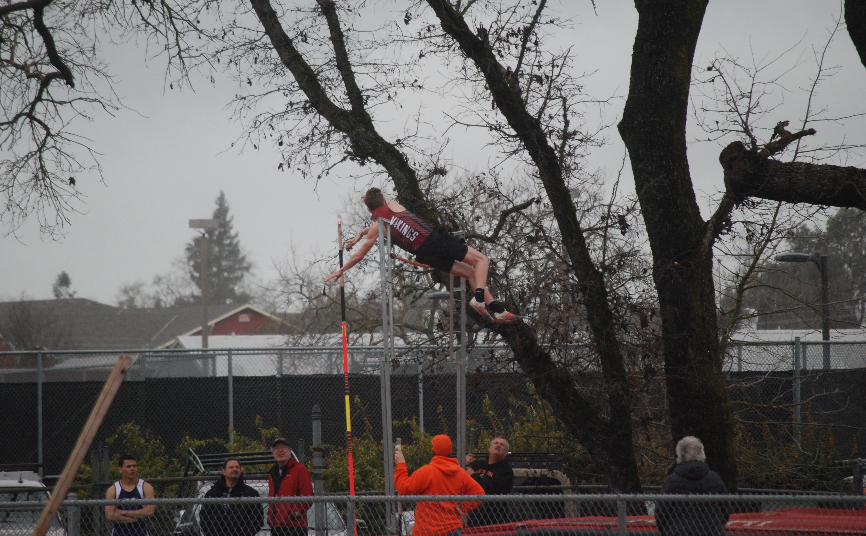 Athlete prepares for pole vault on a track with others watching.