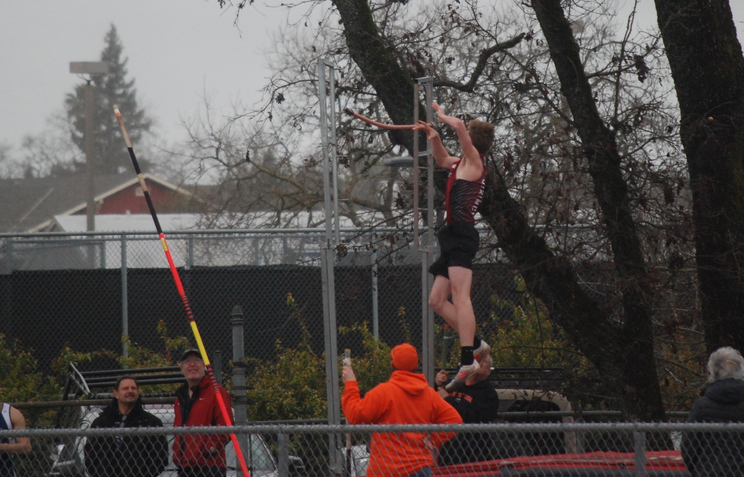 Athlete prepares for pole vault on a track with others watching.