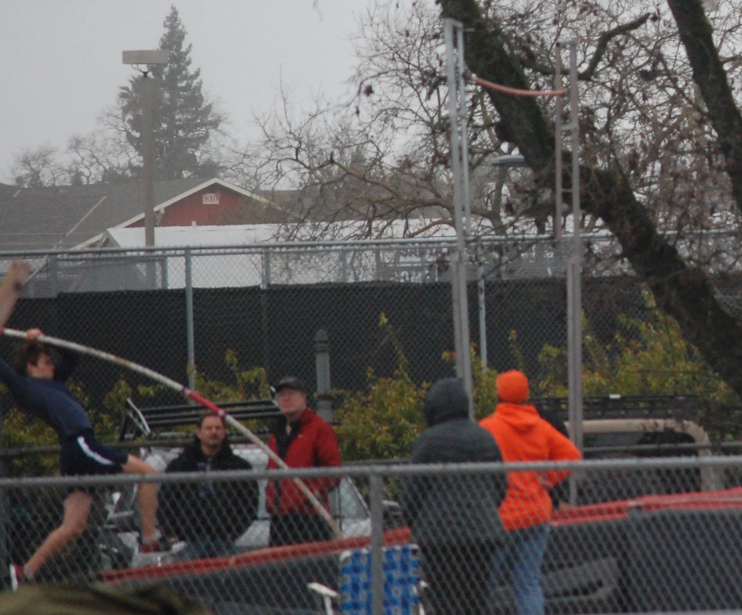 Athlete prepares for pole vault on a track with others watching.