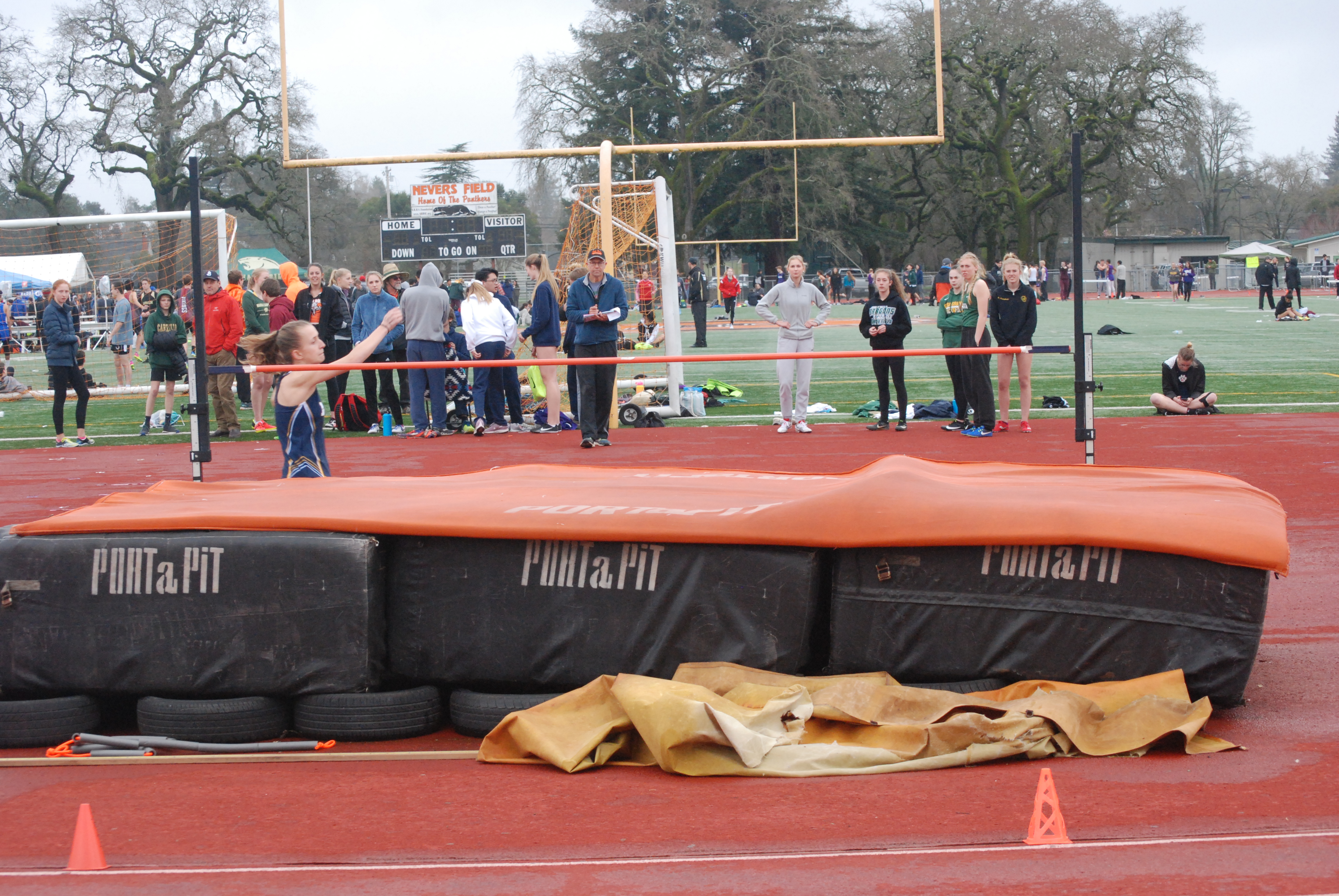 Athlete prepares for pole vault on a track with others watching.