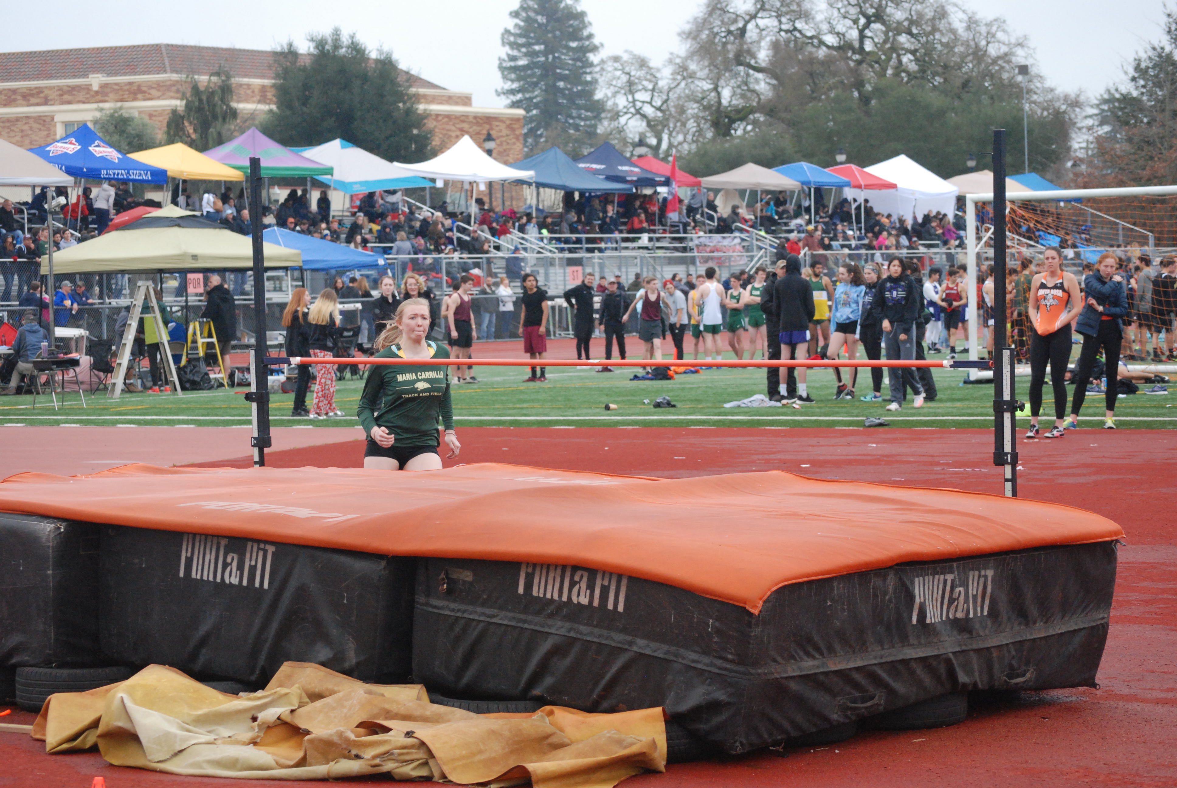 Athlete prepares for pole vault on a track with others watching.