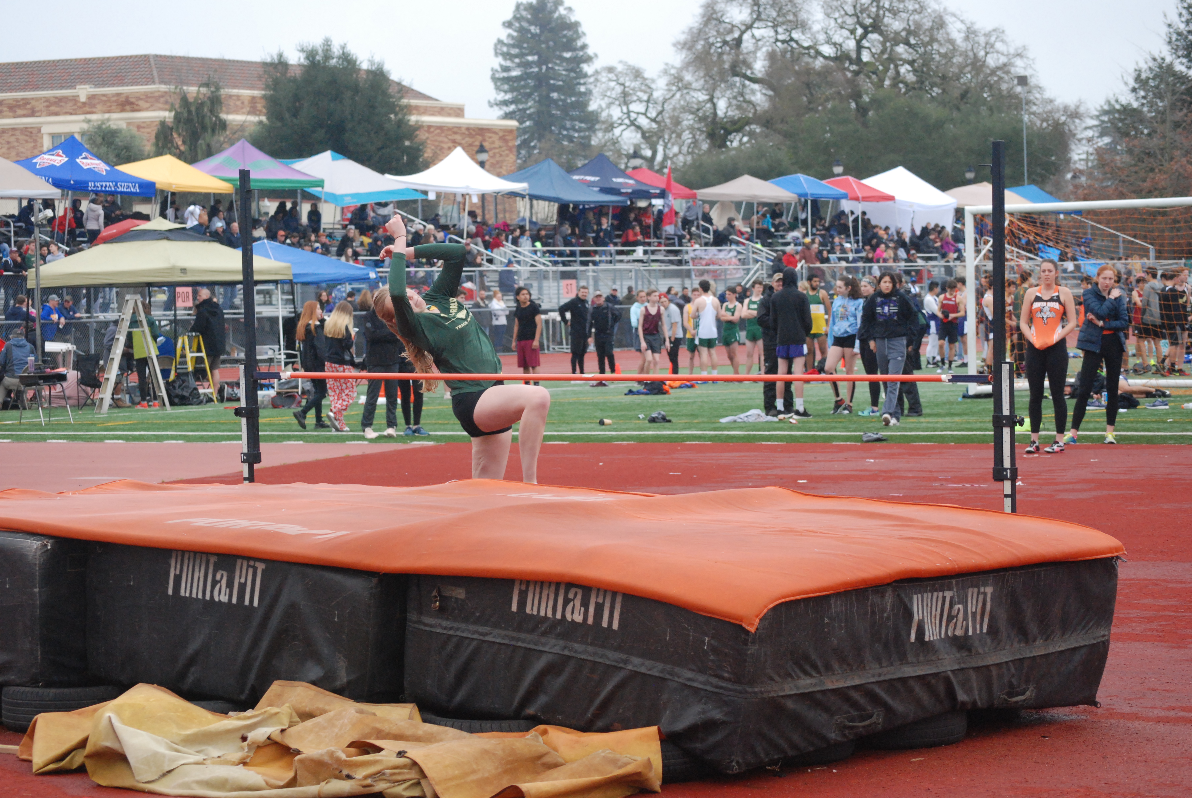 Athlete prepares for pole vault on a track with others watching.