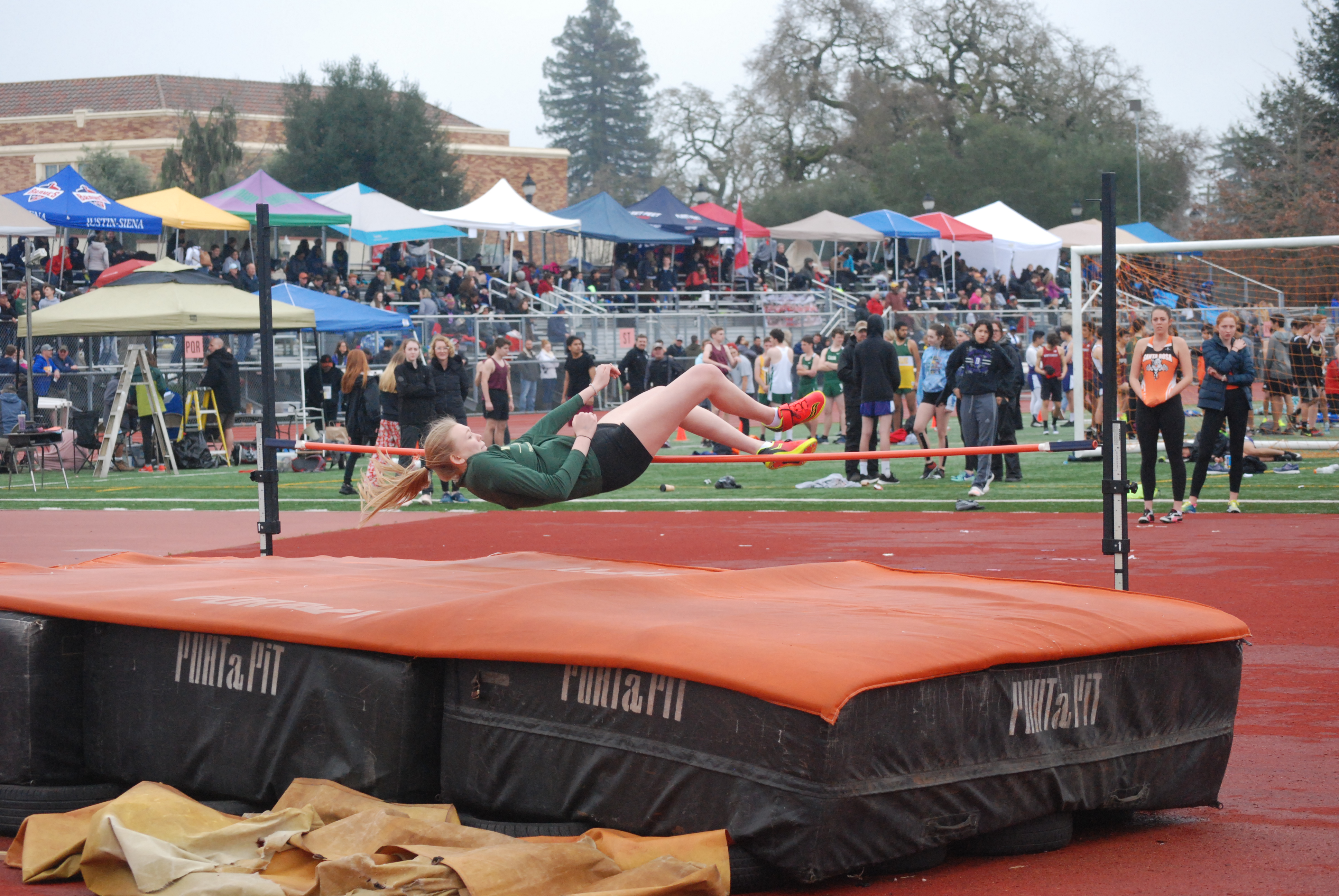 Athlete prepares for pole vault on a track with others watching.