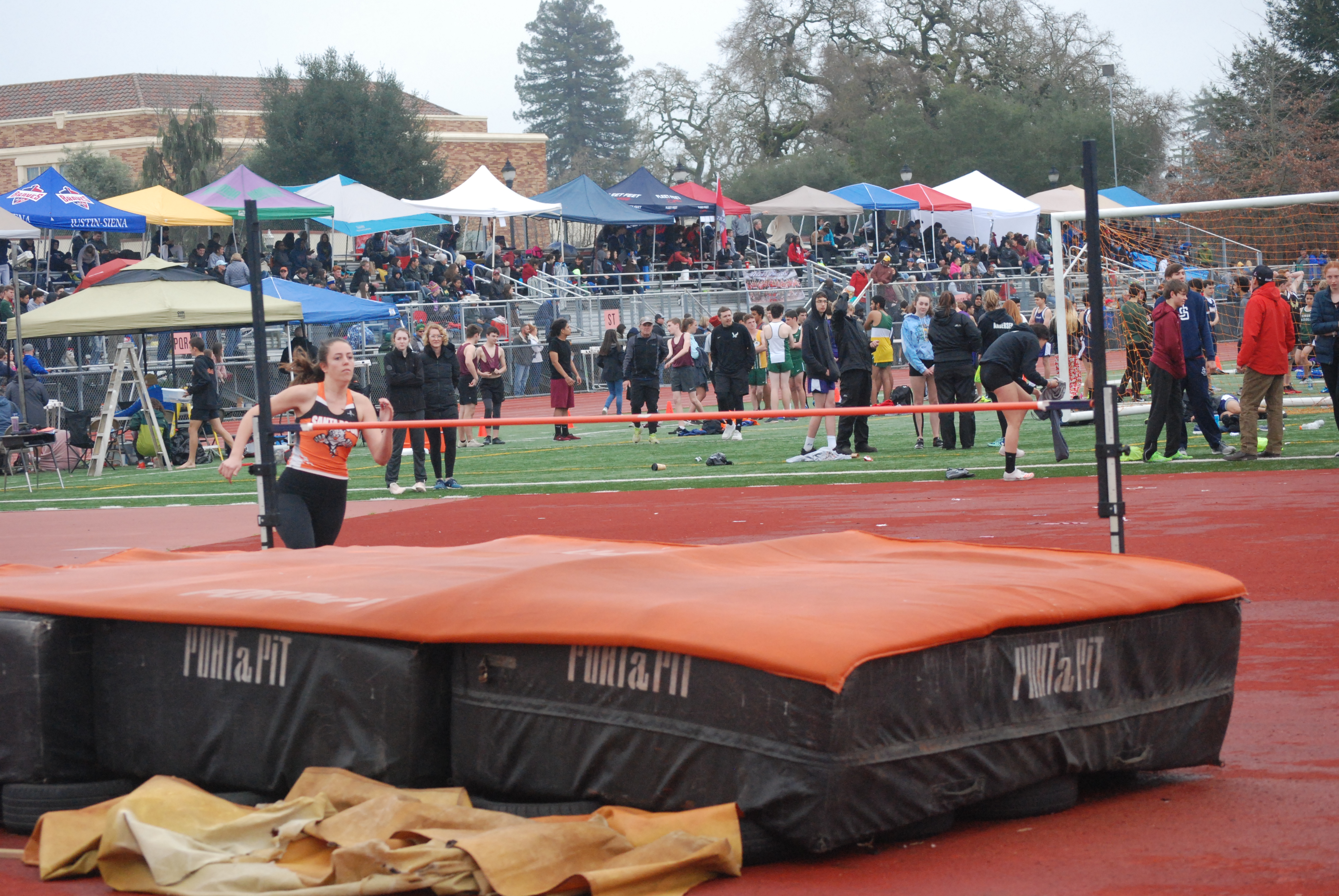 Athlete prepares for pole vault on a track with others watching.