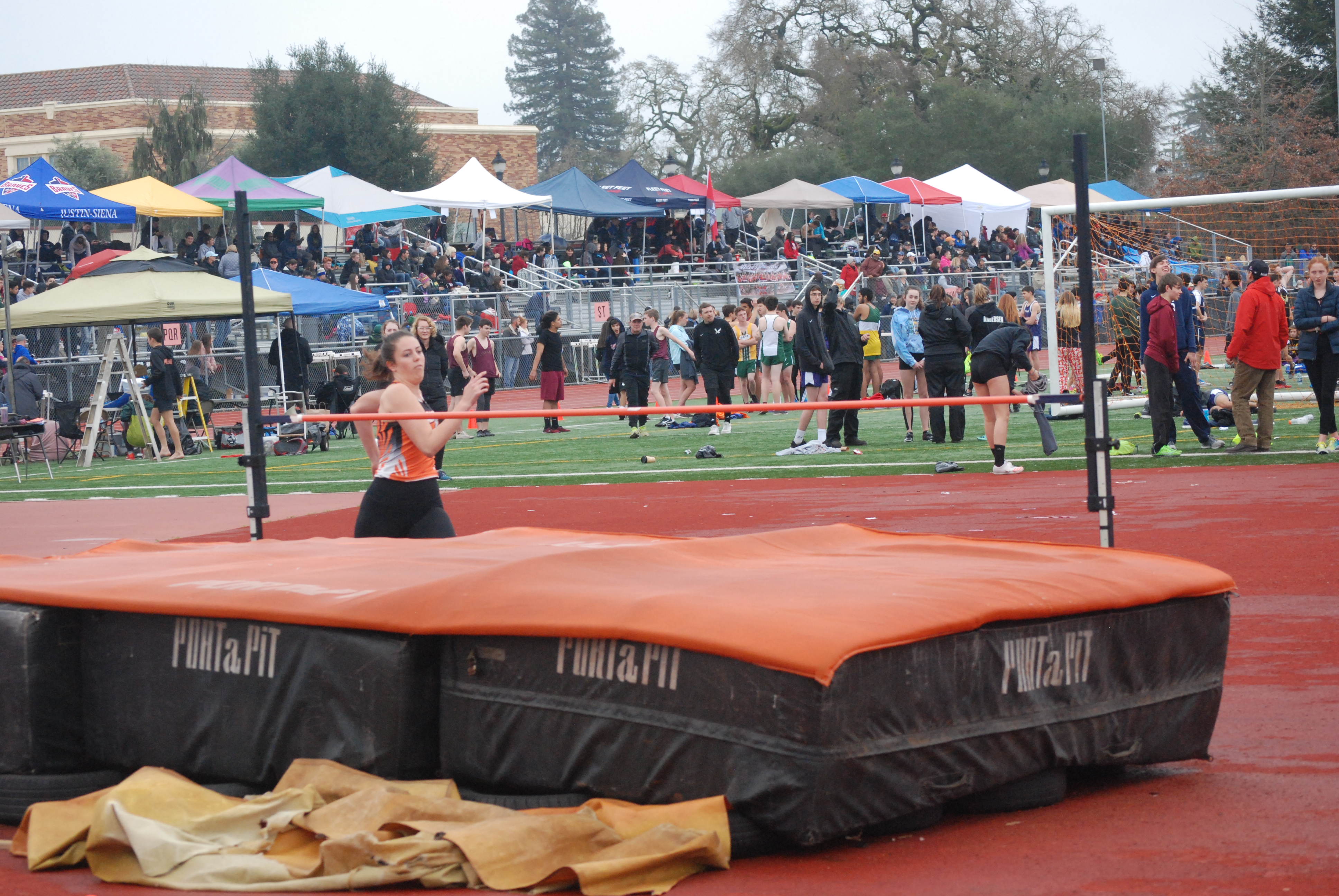 Athlete prepares for pole vault on a track with others watching.