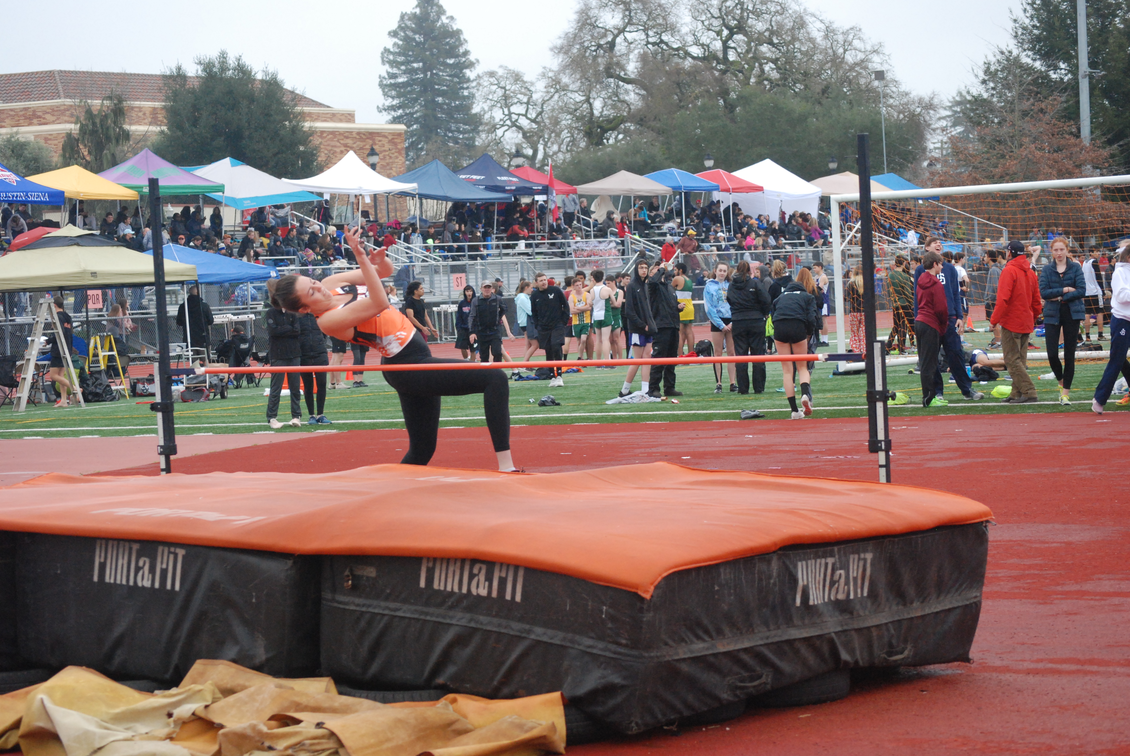 Athlete prepares for pole vault on a track with others watching.