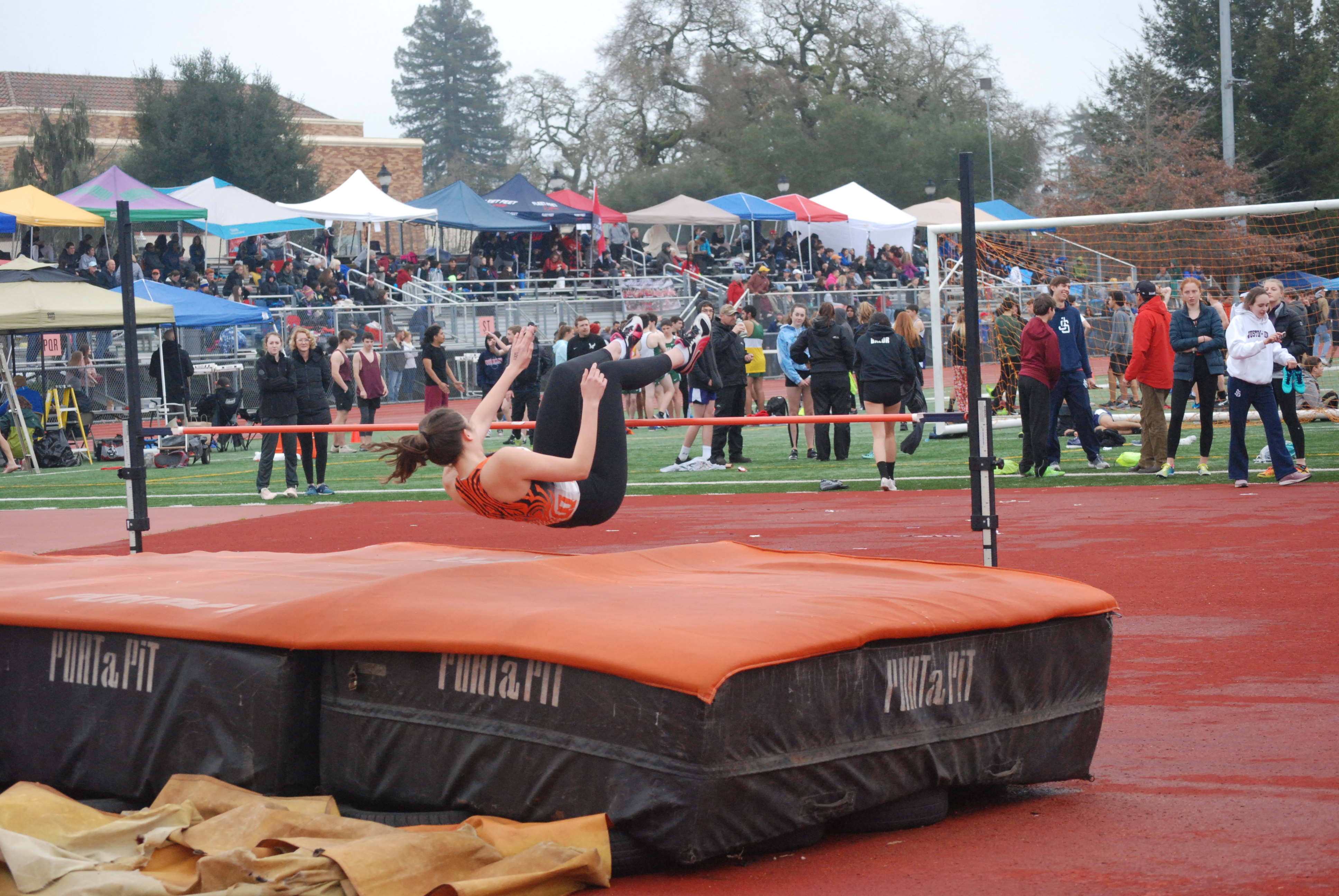 Athlete prepares for pole vault on a track with others watching.