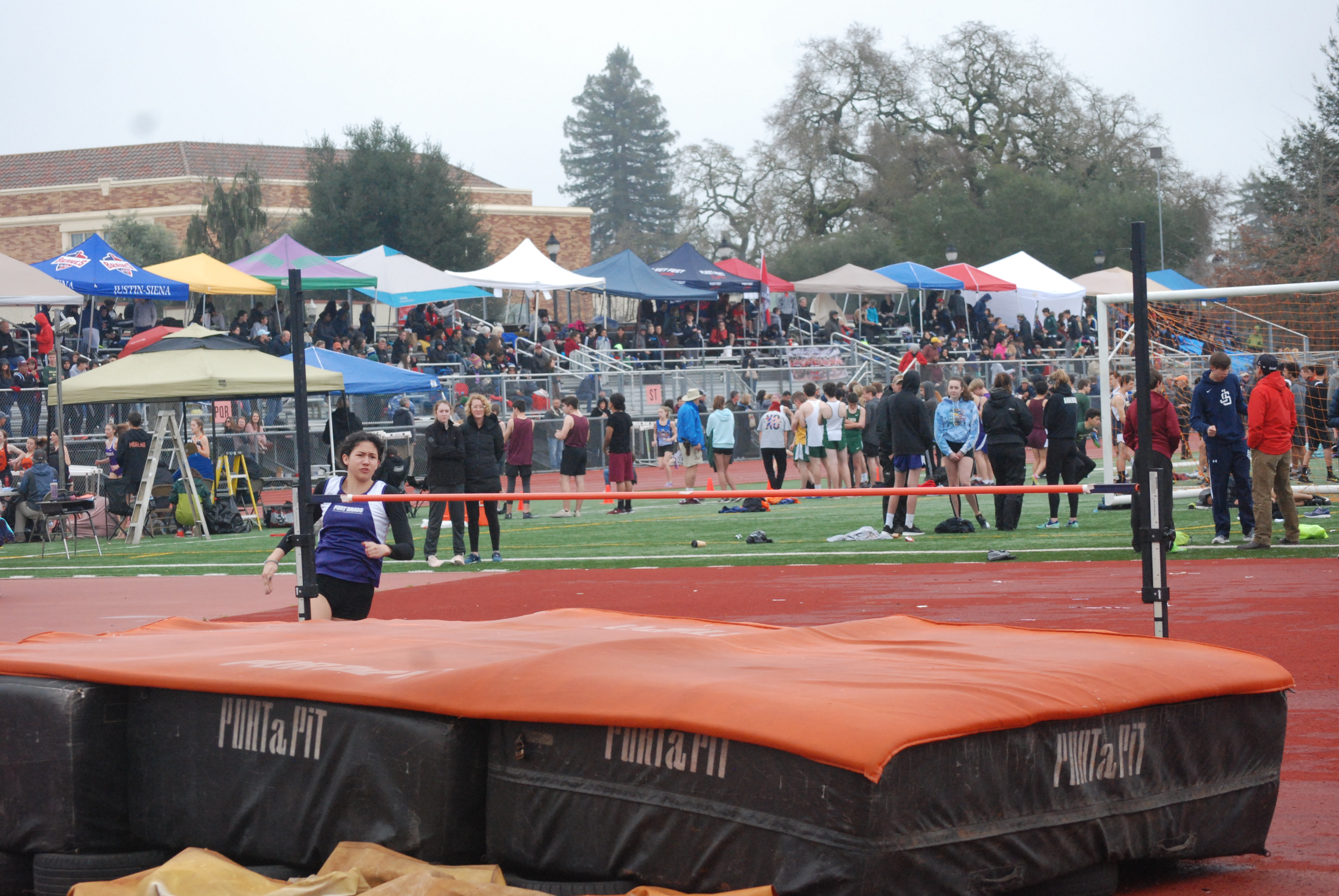 Athlete prepares for pole vault on a track with others watching.