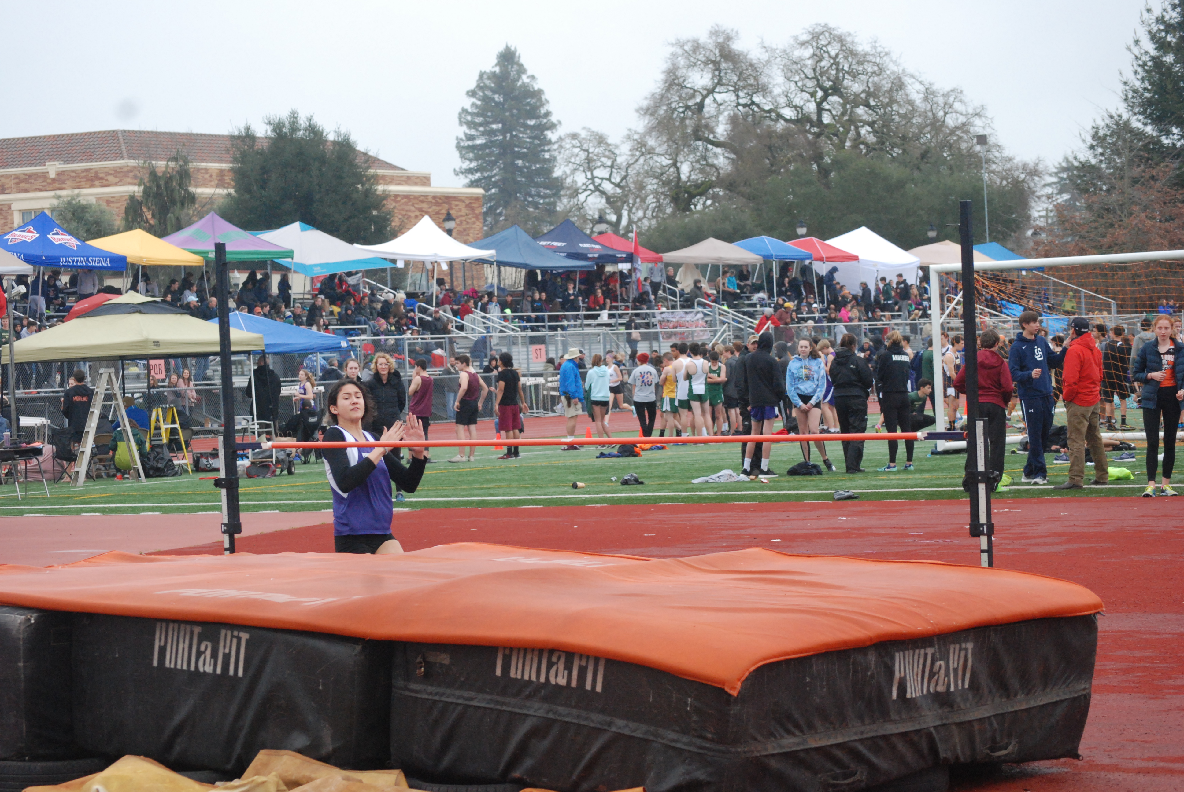 Athlete prepares for pole vault on a track with others watching.