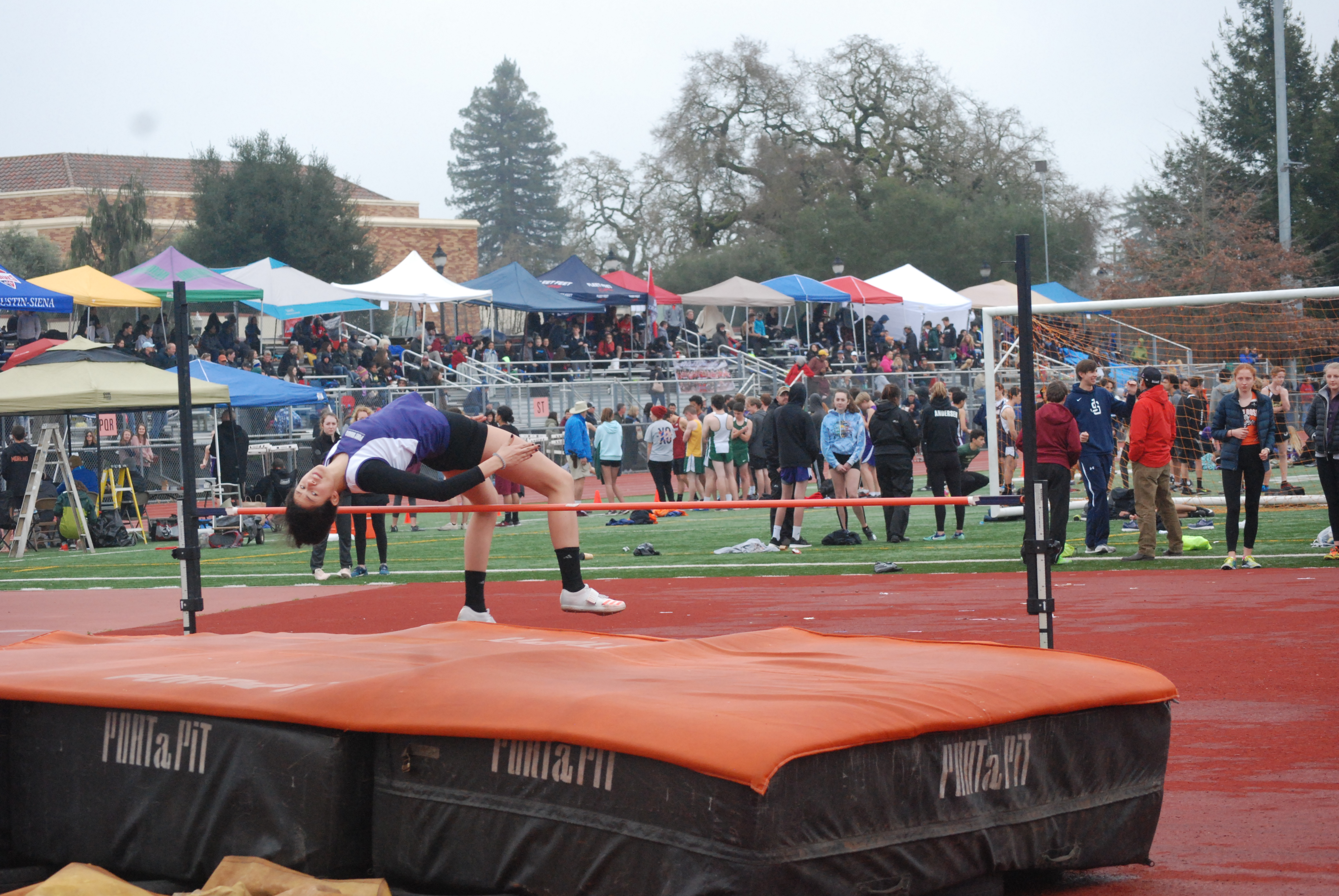 Athlete prepares for pole vault on a track with others watching.