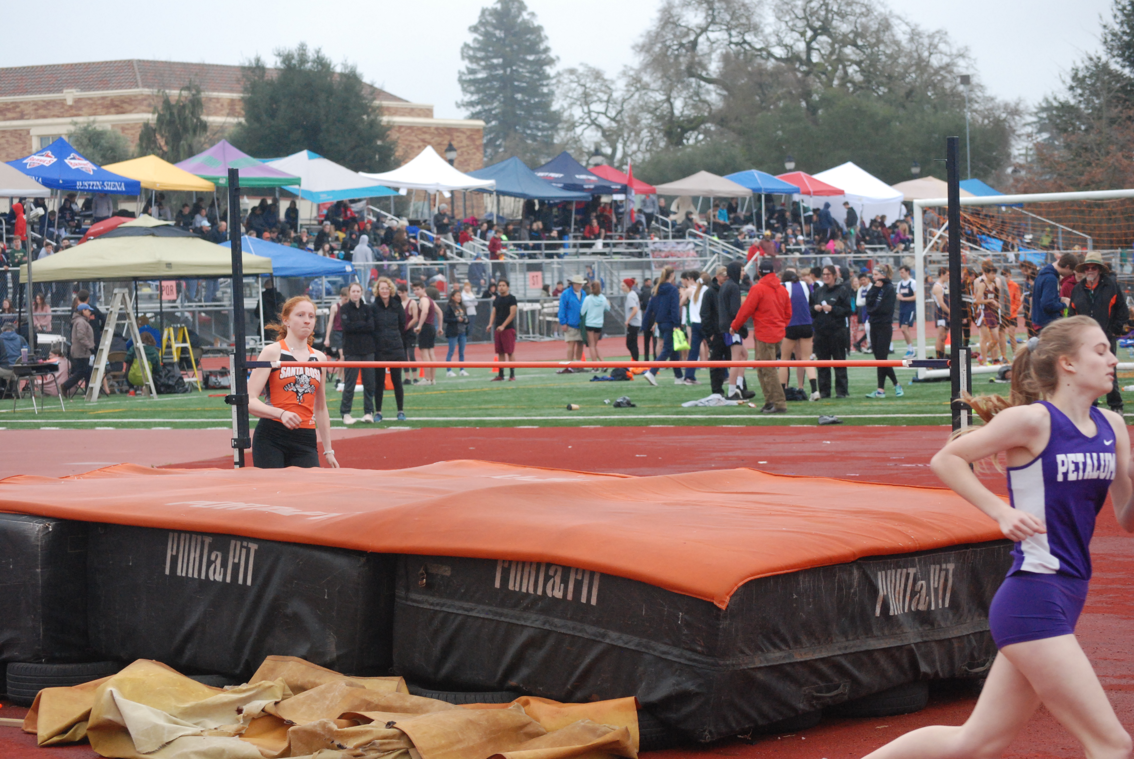 Athlete prepares for pole vault on a track with others watching.