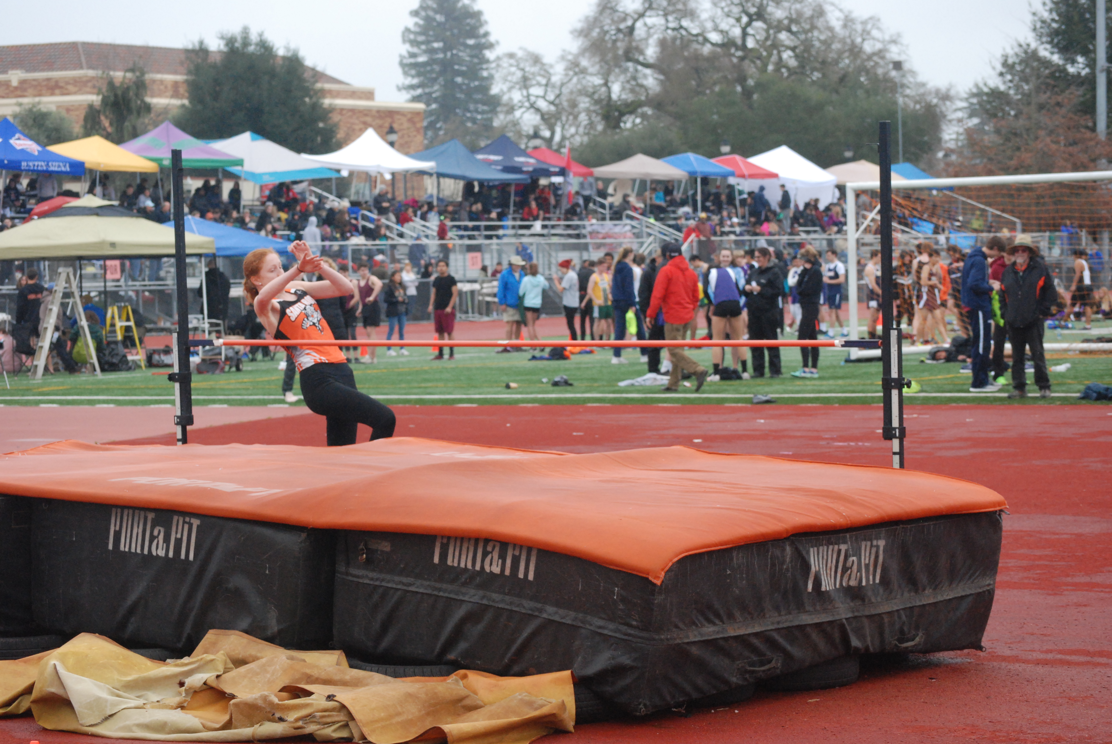 Athlete prepares for pole vault on a track with others watching.