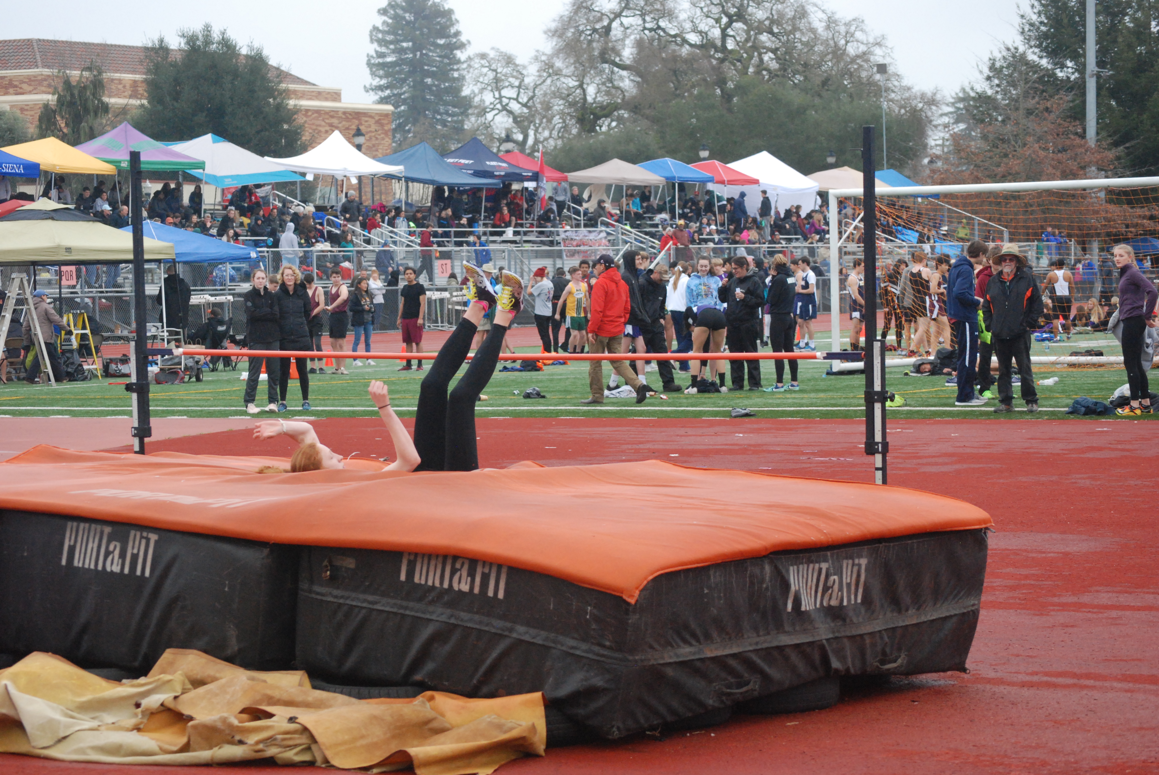 Athlete prepares for pole vault on a track with others watching.