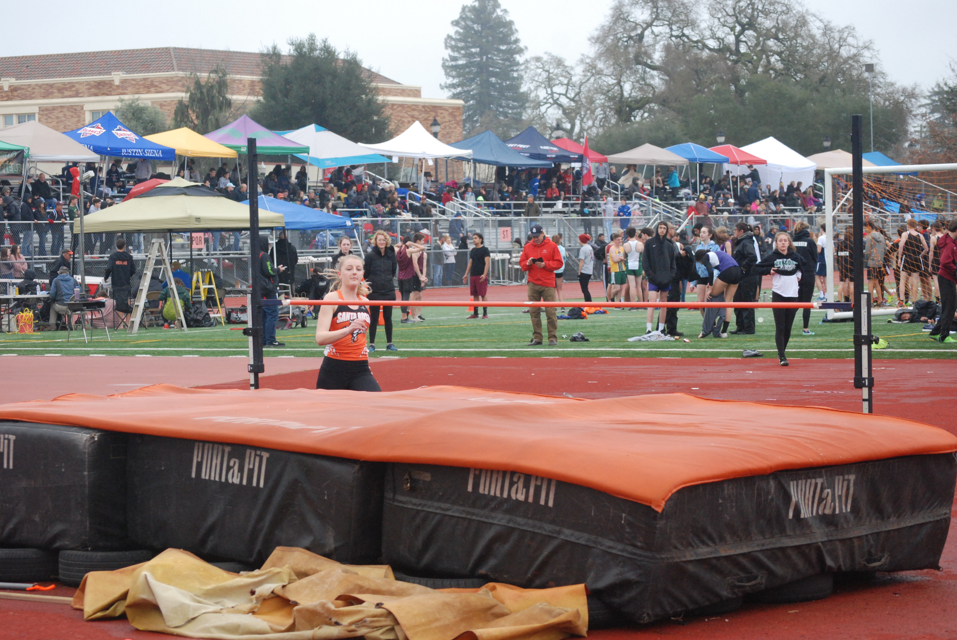 Athlete prepares for pole vault on a track with others watching.