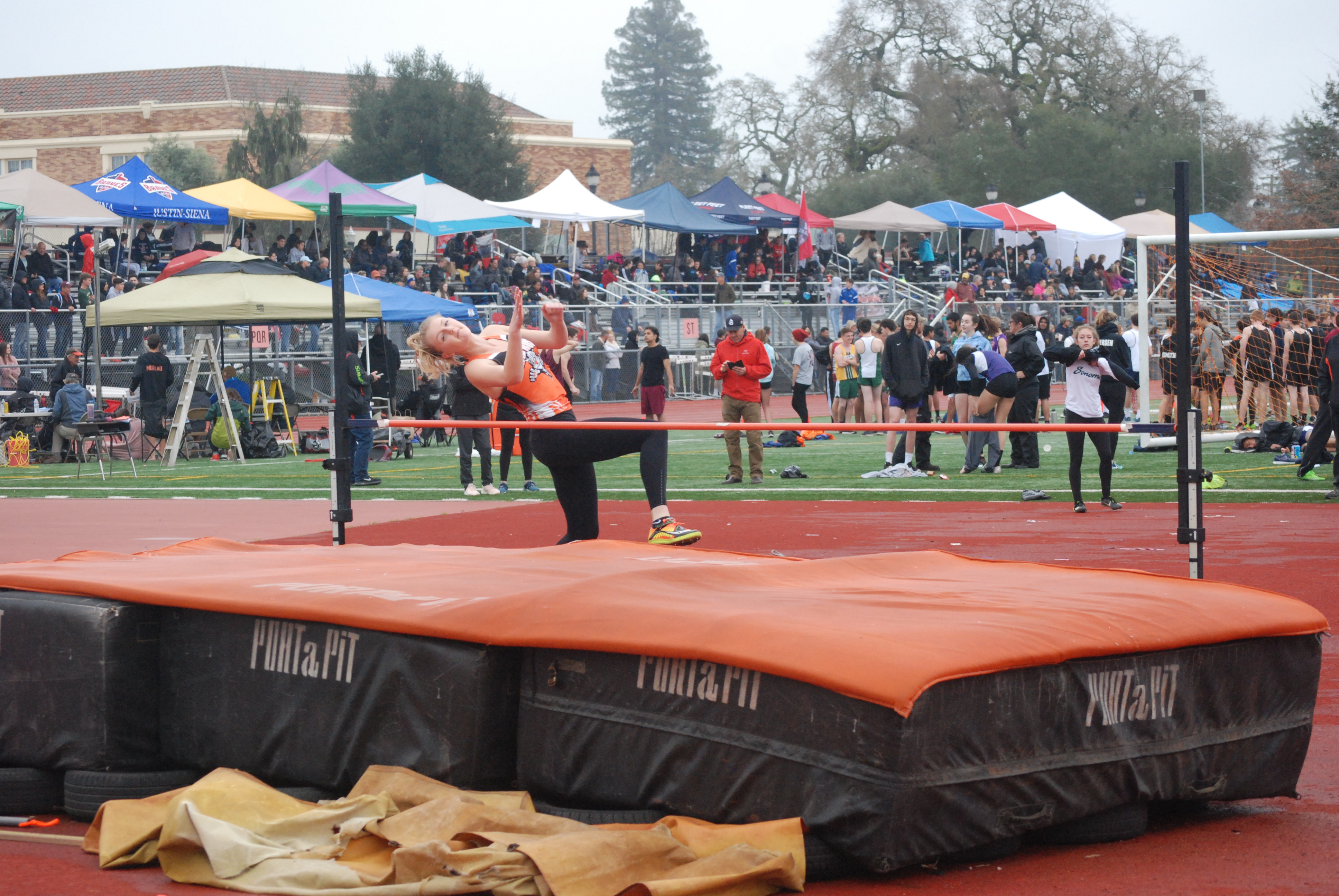 Athlete prepares for pole vault on a track with others watching.