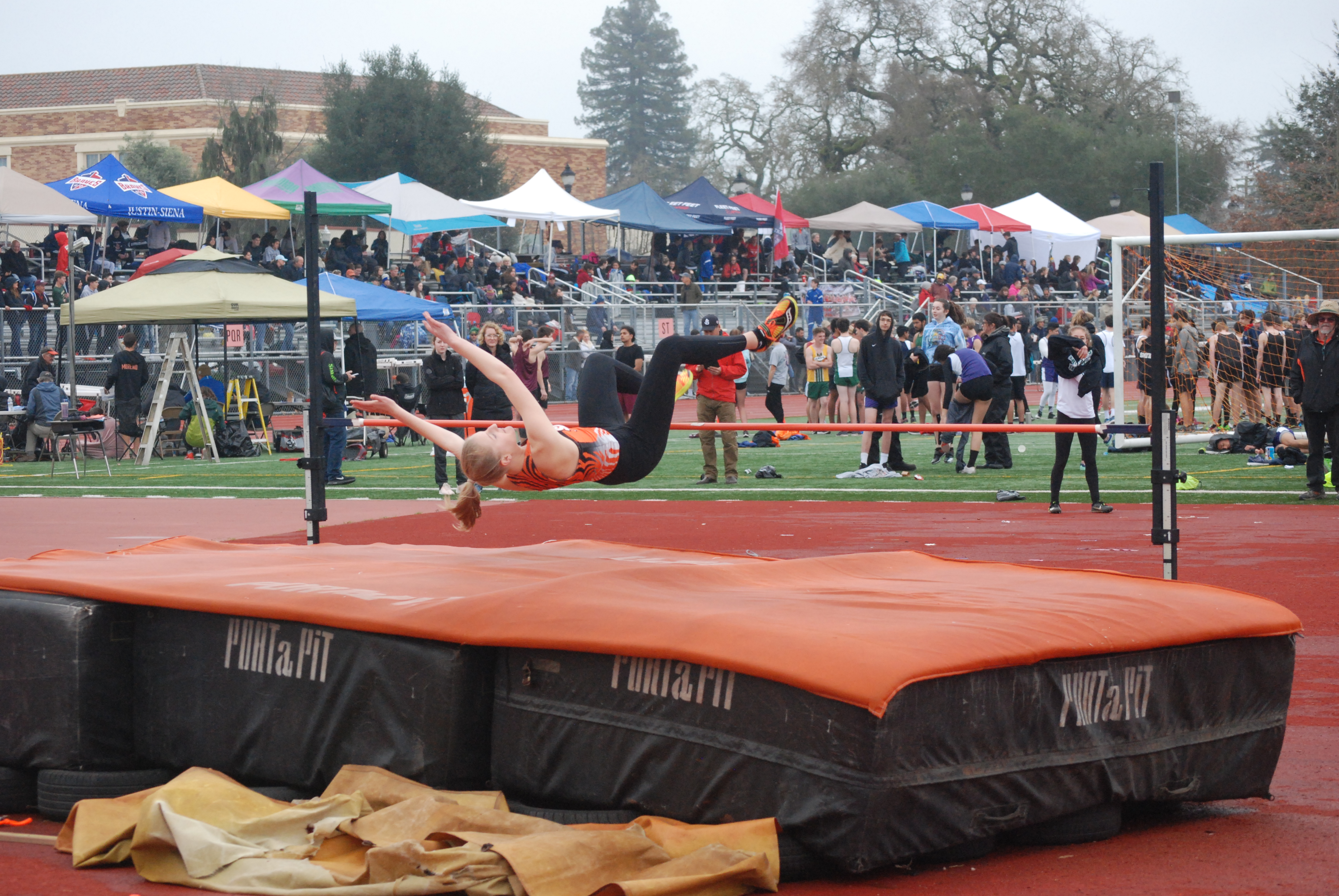 Athlete prepares for pole vault on a track with others watching.