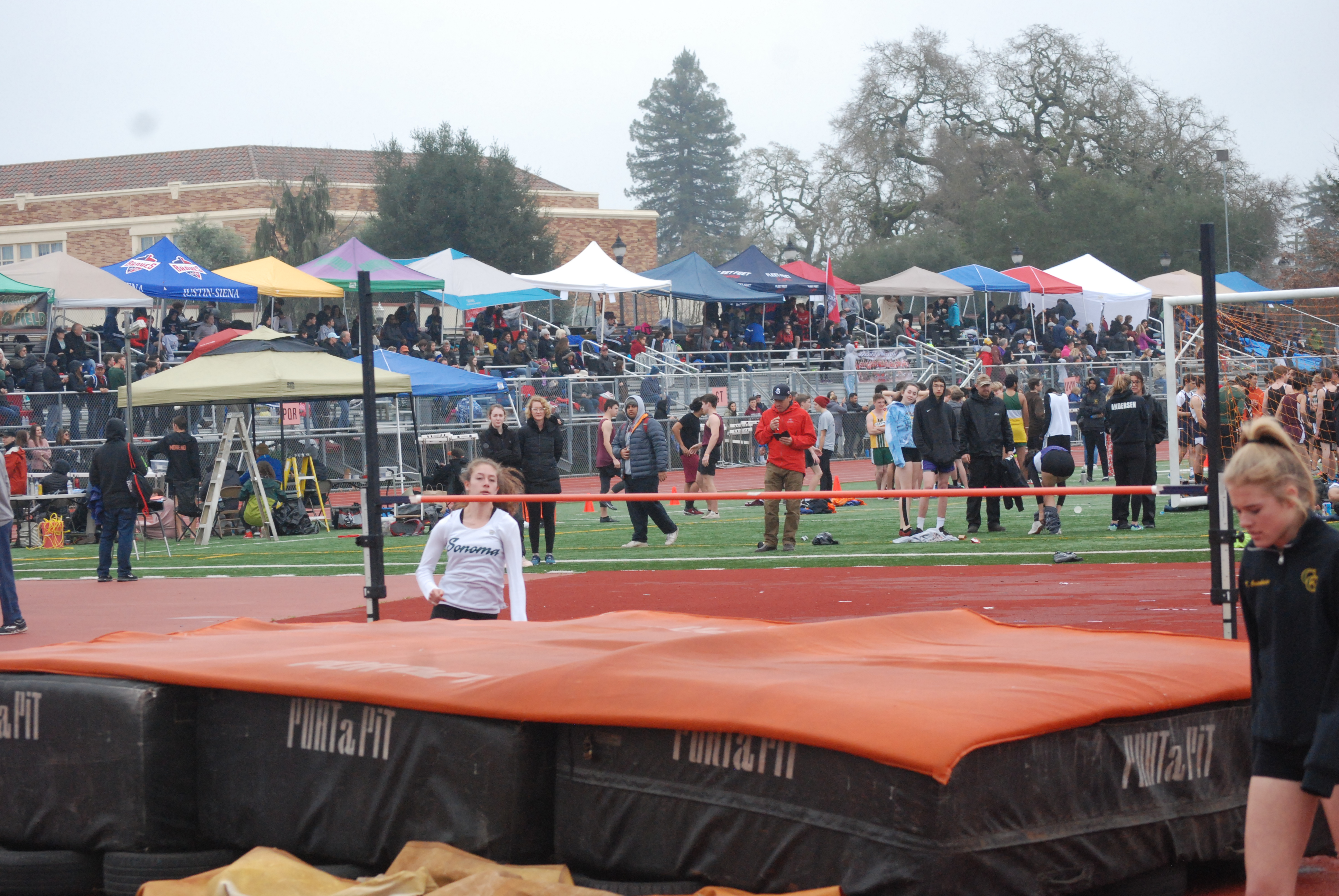 Athlete prepares for pole vault on a track with others watching.