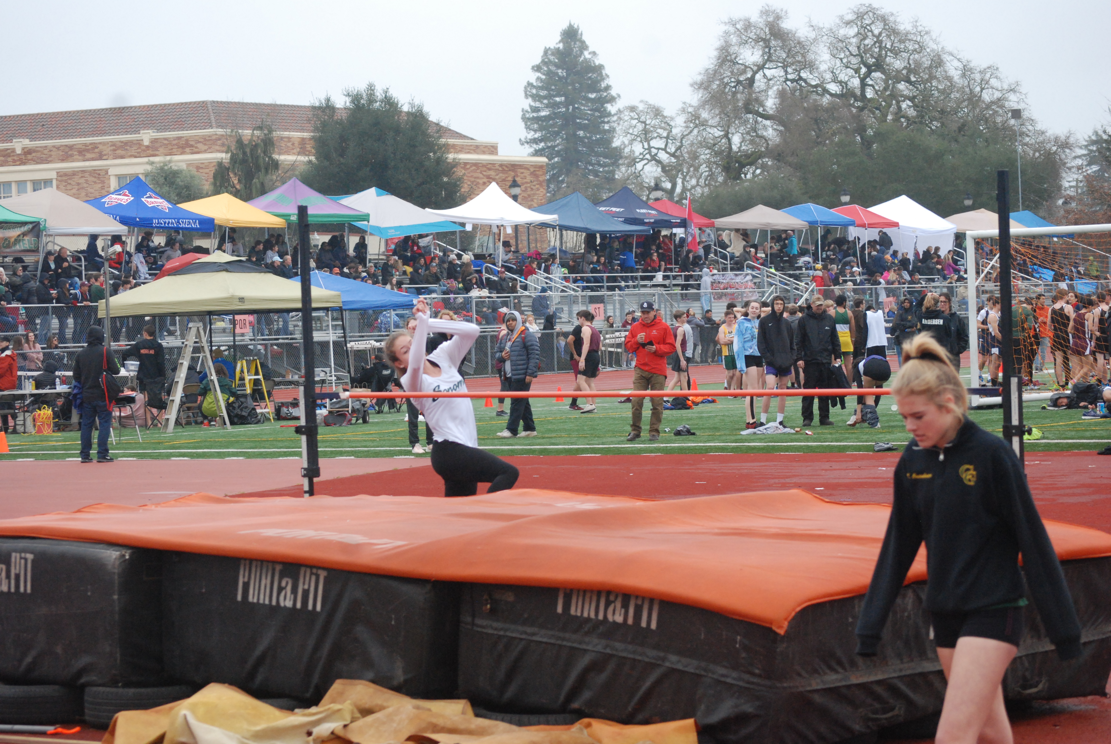 Athlete prepares for pole vault on a track with others watching.