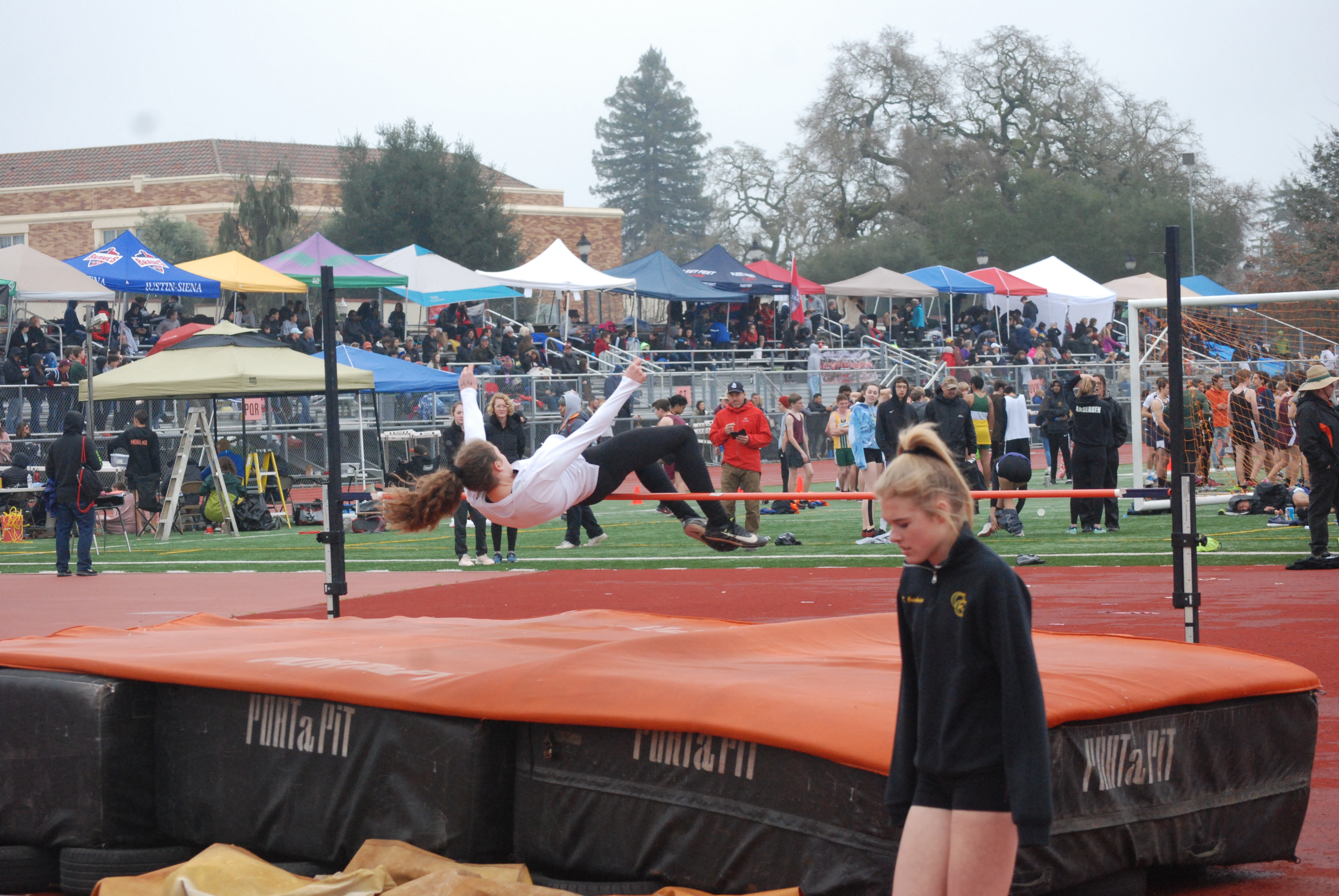 Athlete prepares for pole vault on a track with others watching.