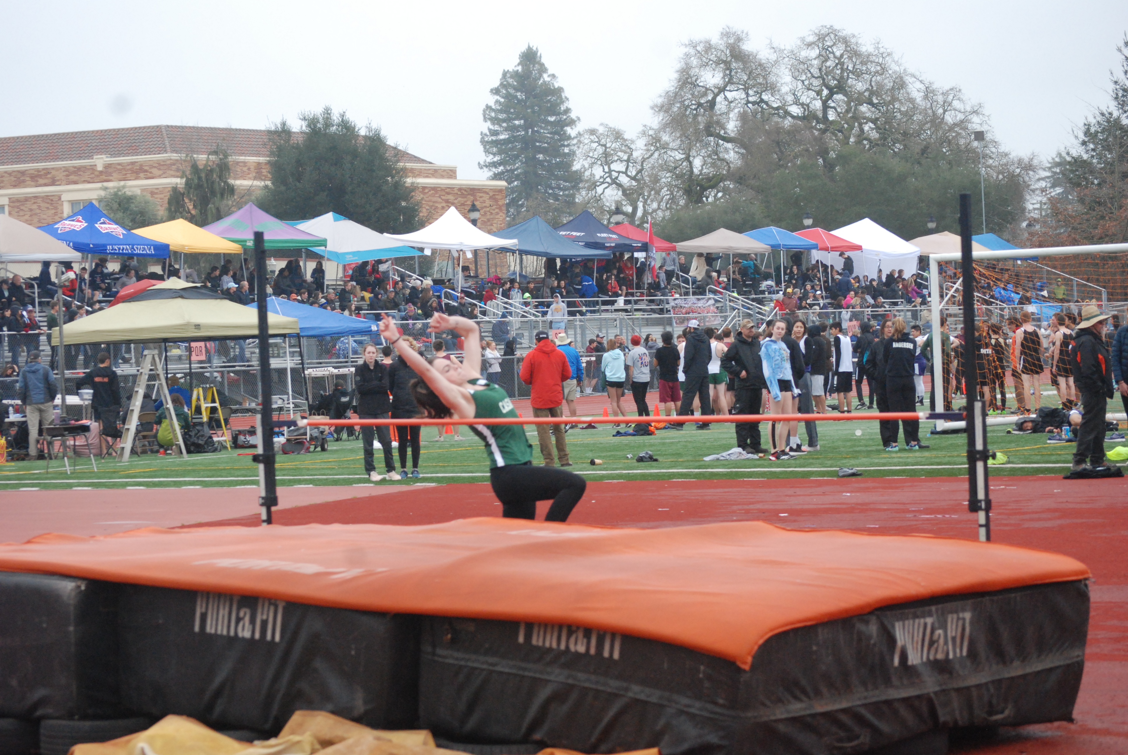 Athlete prepares for pole vault on a track with others watching.