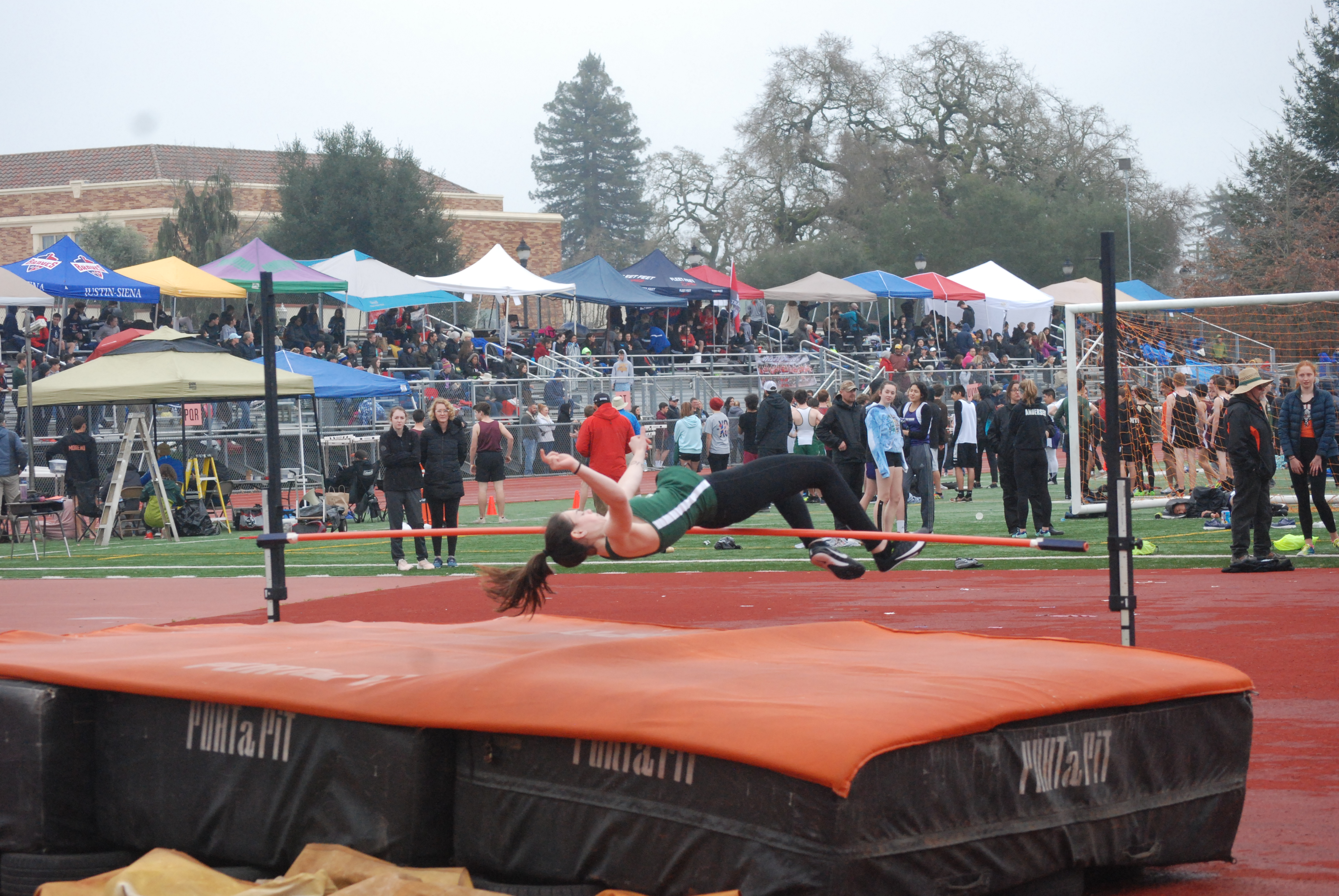 Athlete prepares for pole vault on a track with others watching.