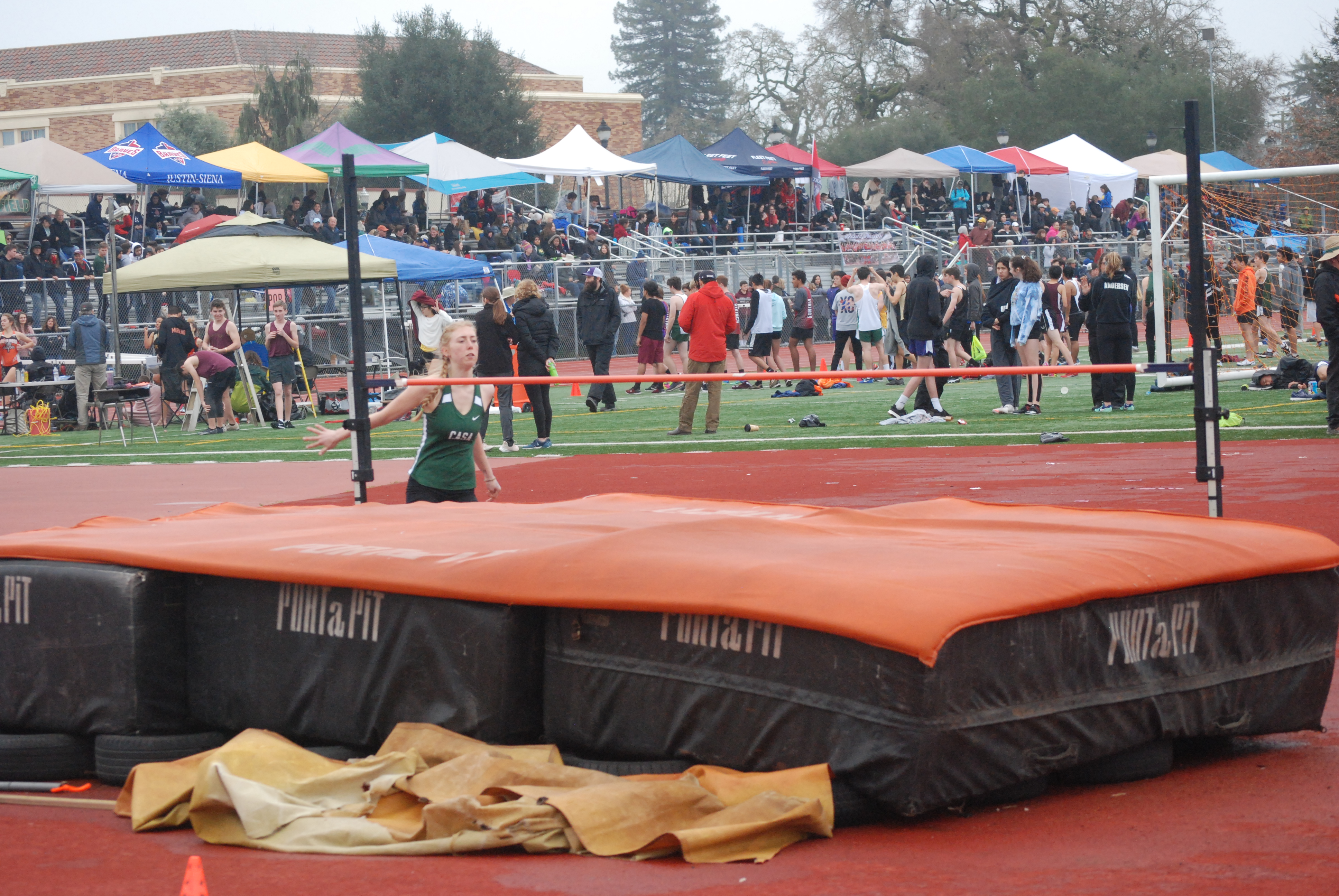 Athlete prepares for pole vault on a track with others watching.