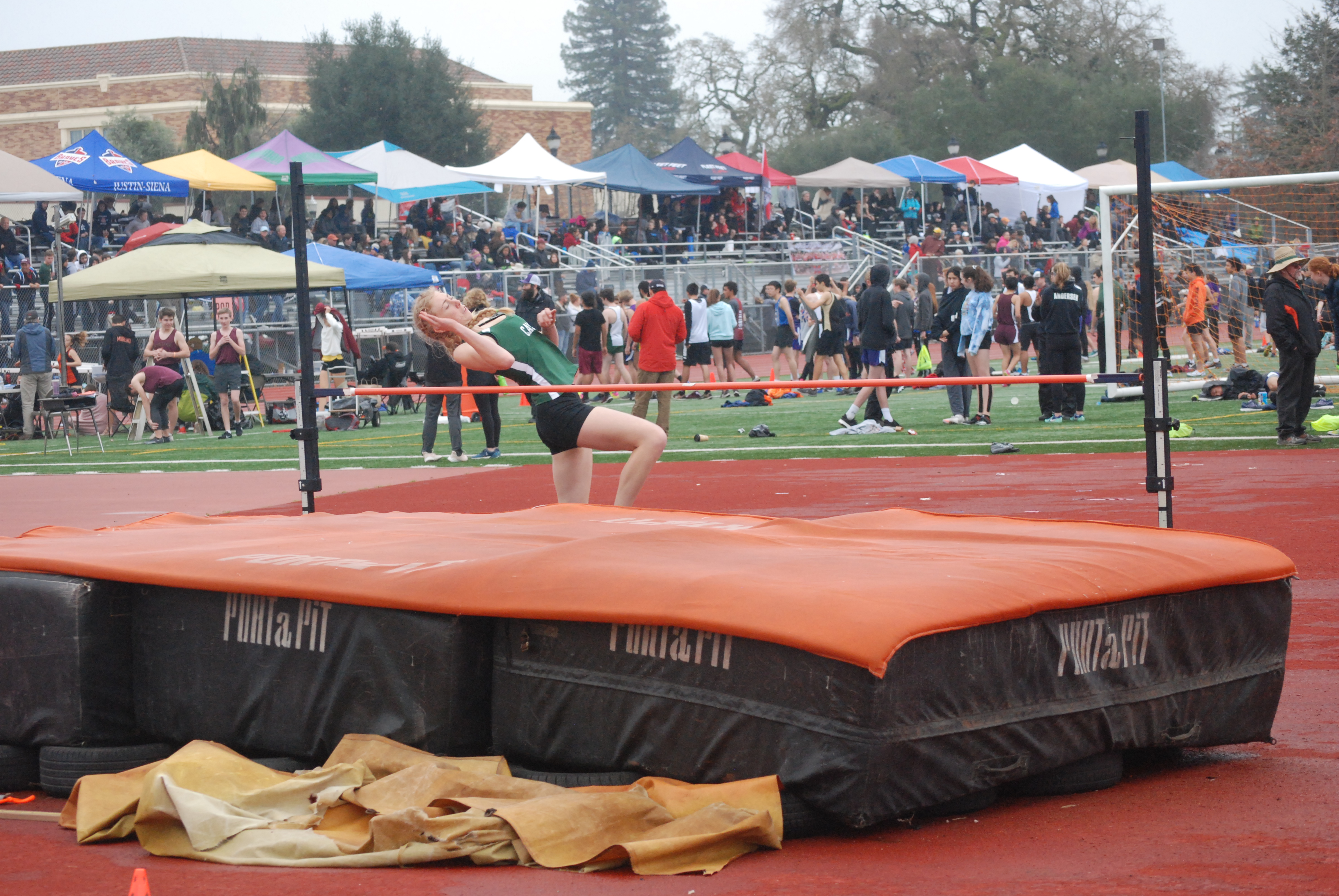 Athlete prepares for pole vault on a track with others watching.