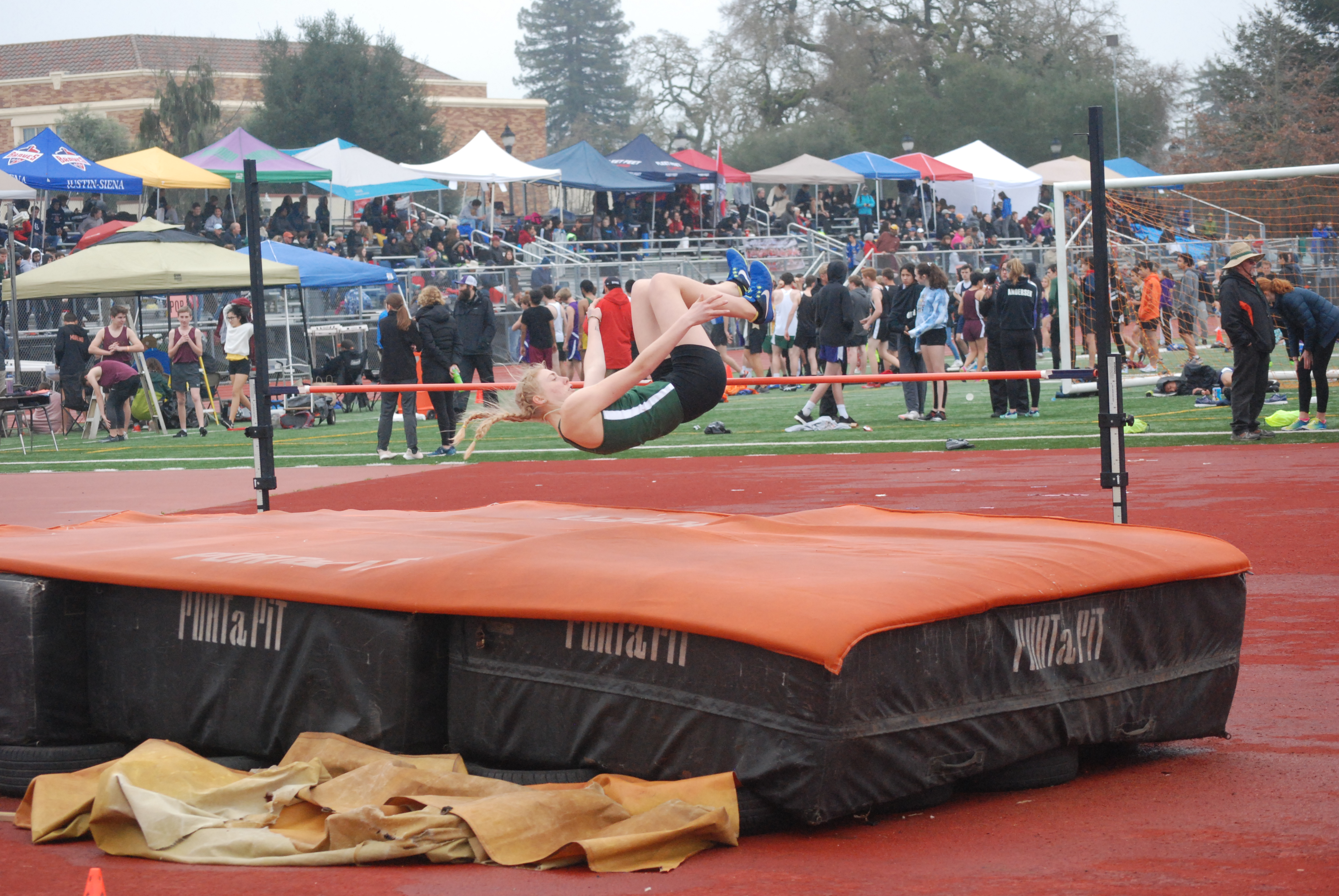 Athlete prepares for pole vault on a track with others watching.