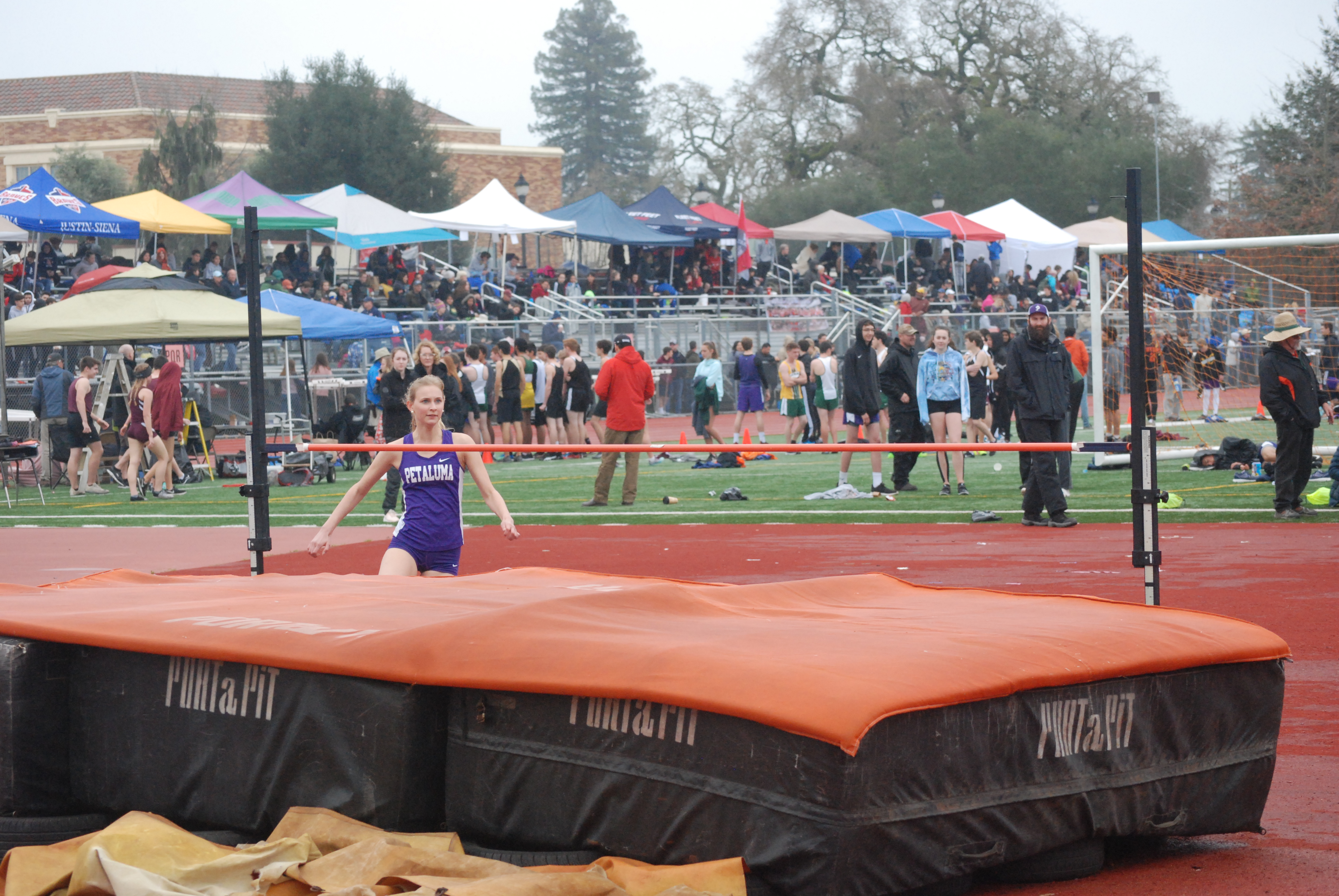 Athlete prepares for pole vault on a track with others watching.