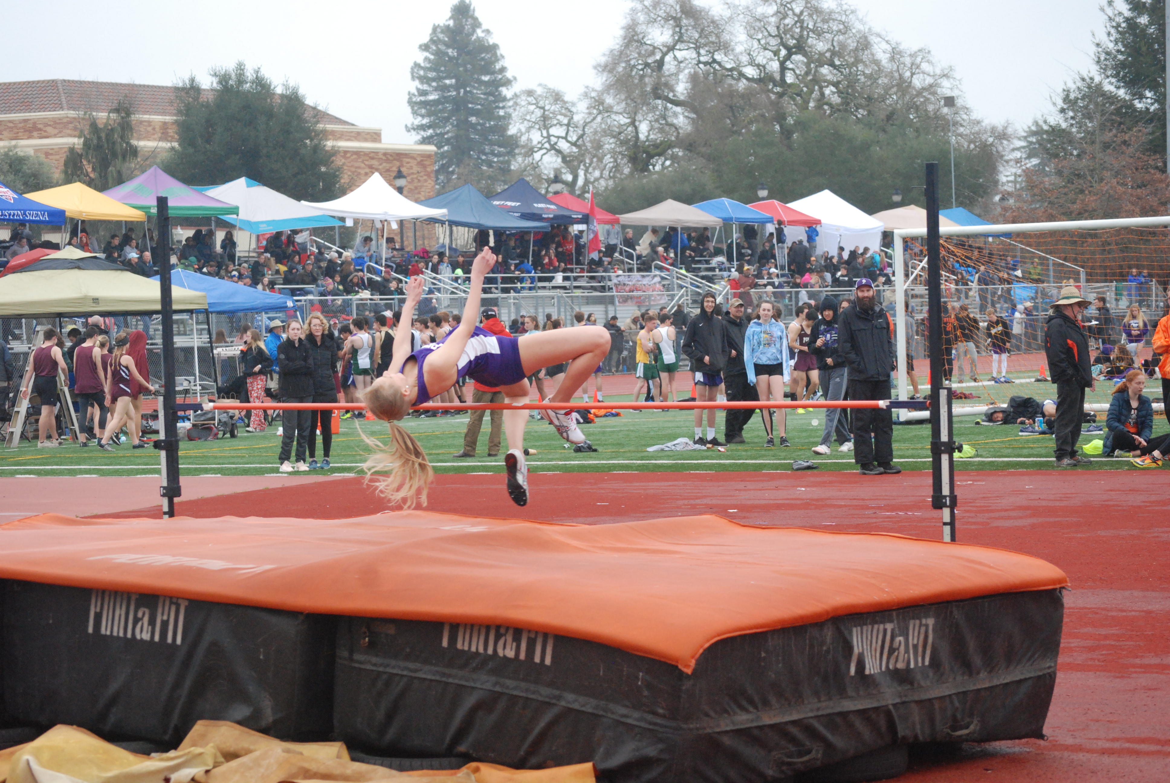 Athlete prepares for pole vault on a track with others watching.