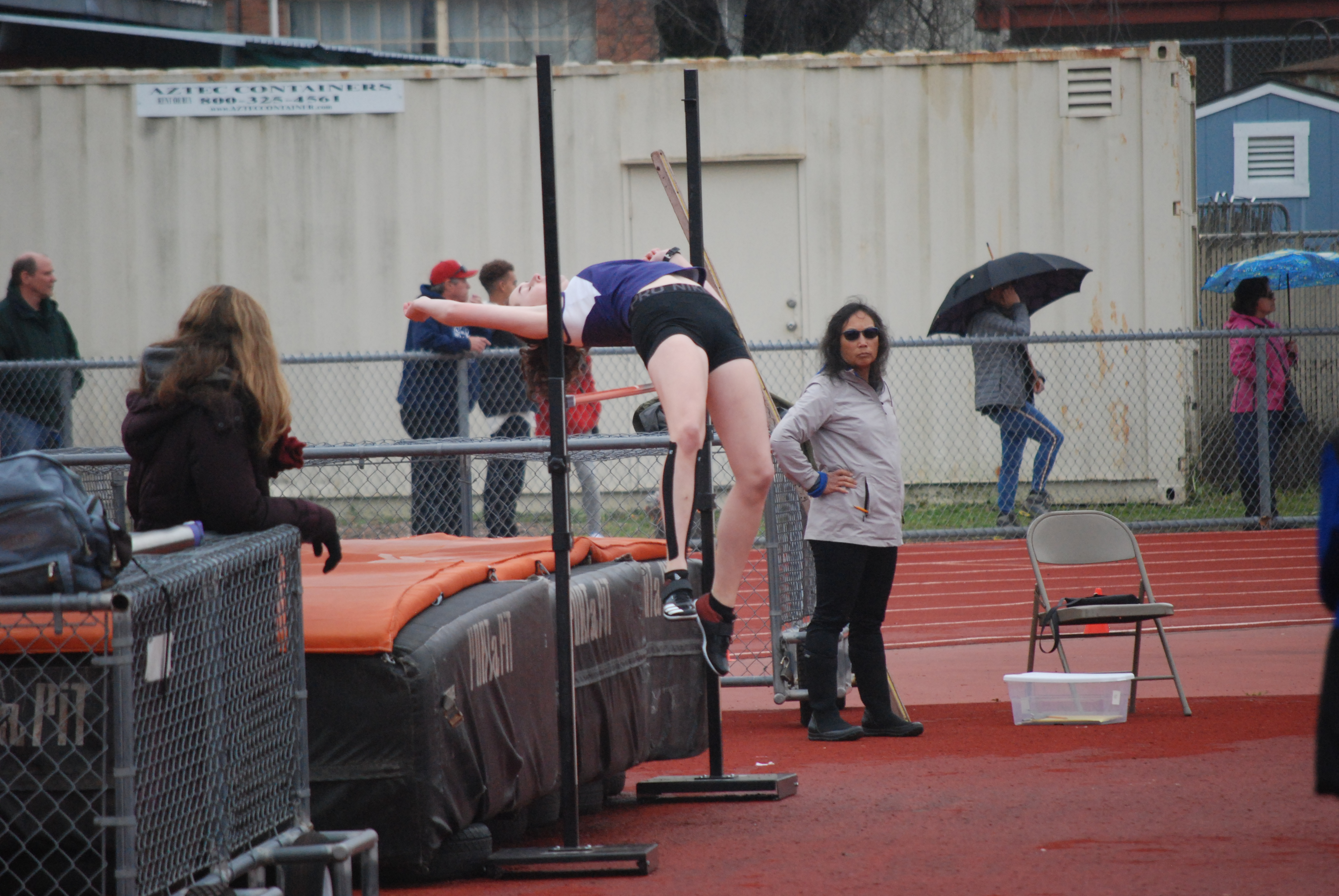 Athlete prepares for pole vault on a track with others watching.