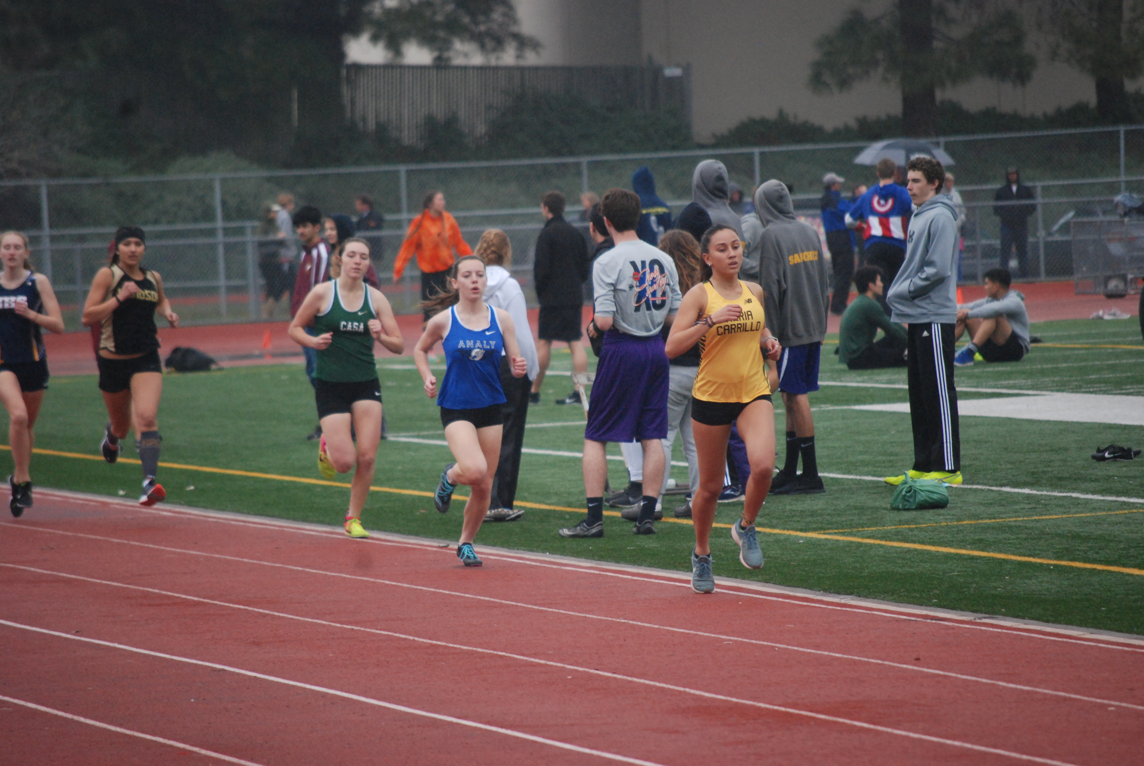 Athlete prepares for pole vault on a track with others watching.