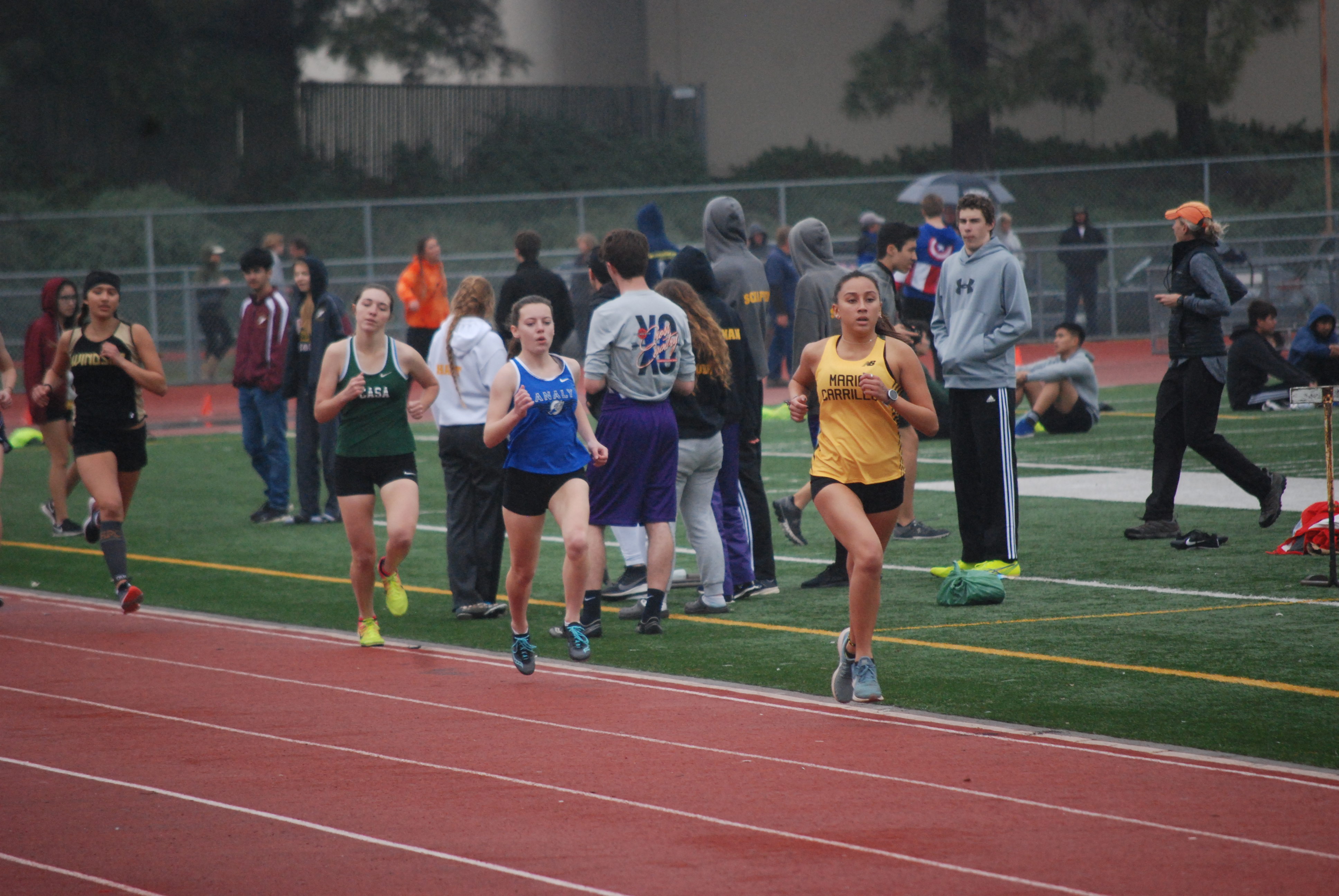 Athlete prepares for pole vault on a track with others watching.