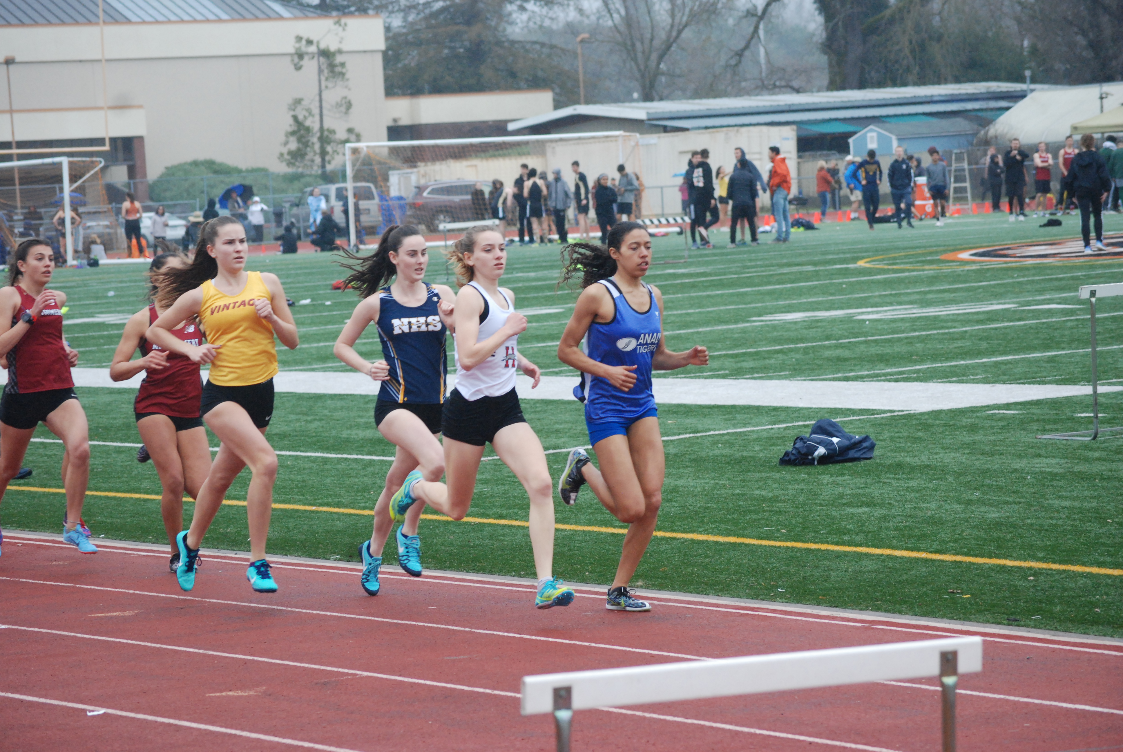 Athlete prepares for pole vault on a track with others watching.