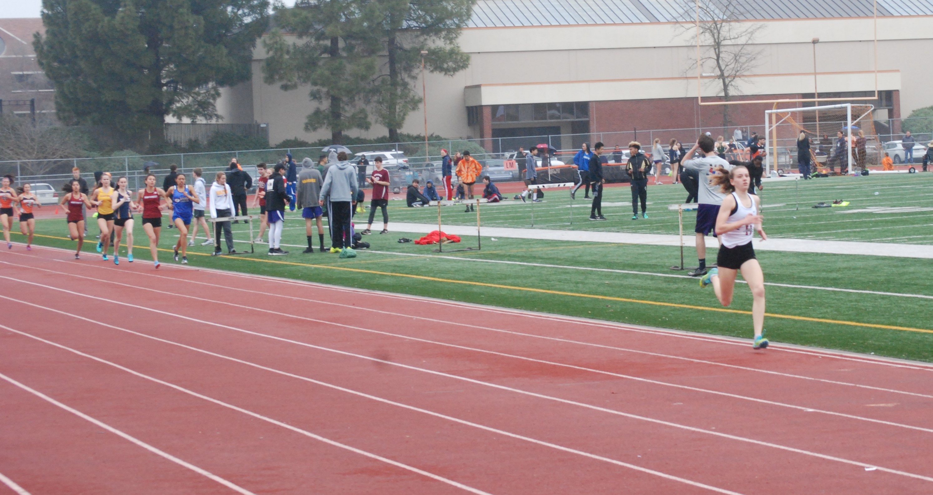 Athlete prepares for pole vault on a track with others watching.