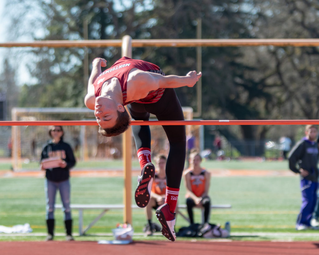 Athlete prepares for pole vault on a track with others watching.