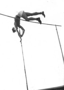 Athlete prepares for pole vault on a track with others watching.