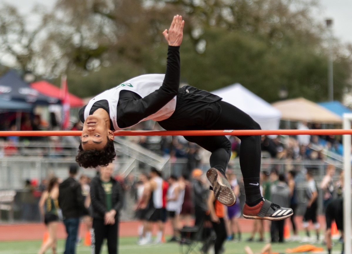 Athlete prepares for pole vault on a track with others watching.