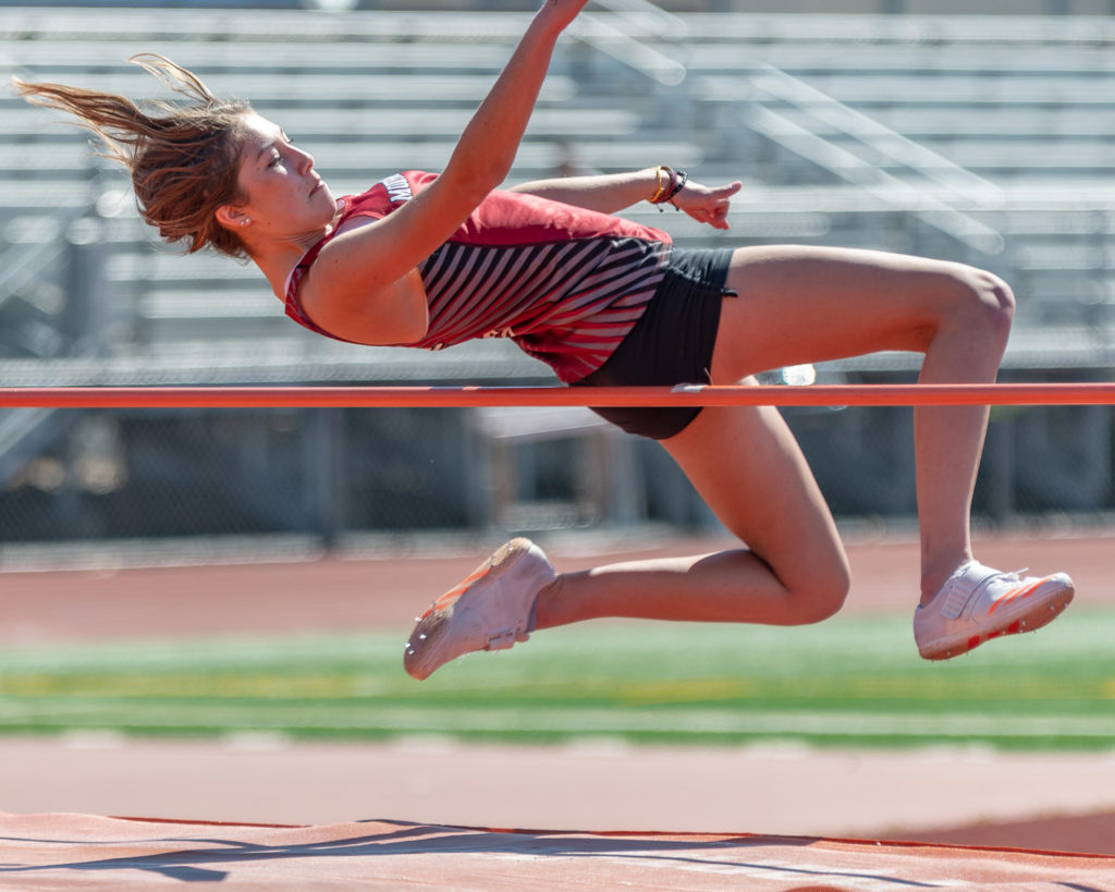 Athlete prepares for pole vault on a track with others watching.