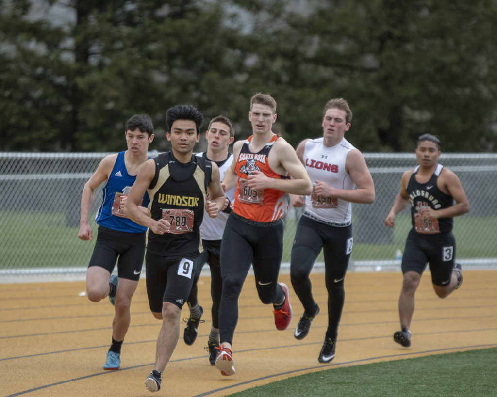 Athlete prepares for pole vault on a track with others watching.